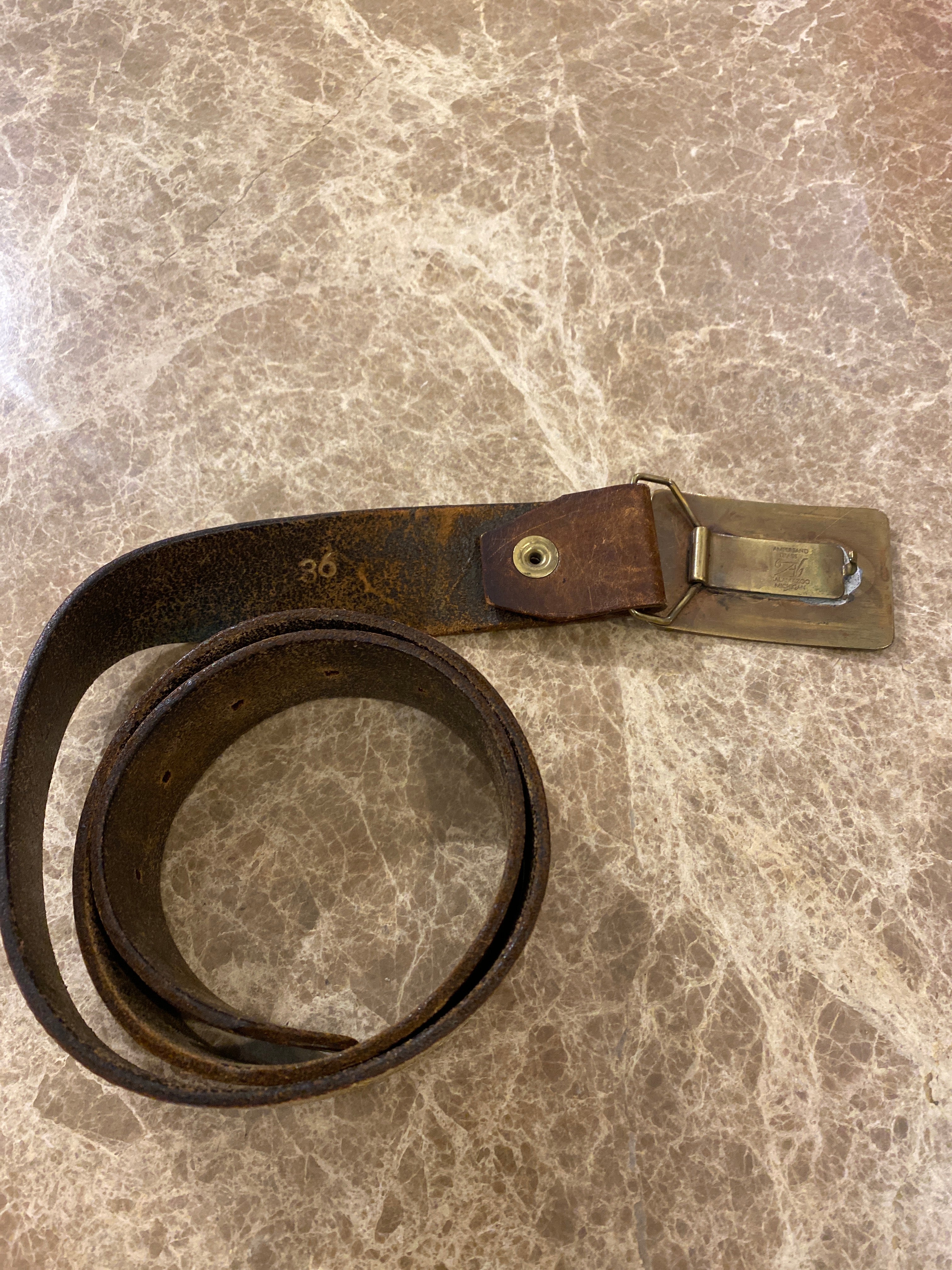 Vintage leather belt with an Ampersand Brass skier buckle.  Rear of belt, shown on a brown & cream Ceasarstone bench.