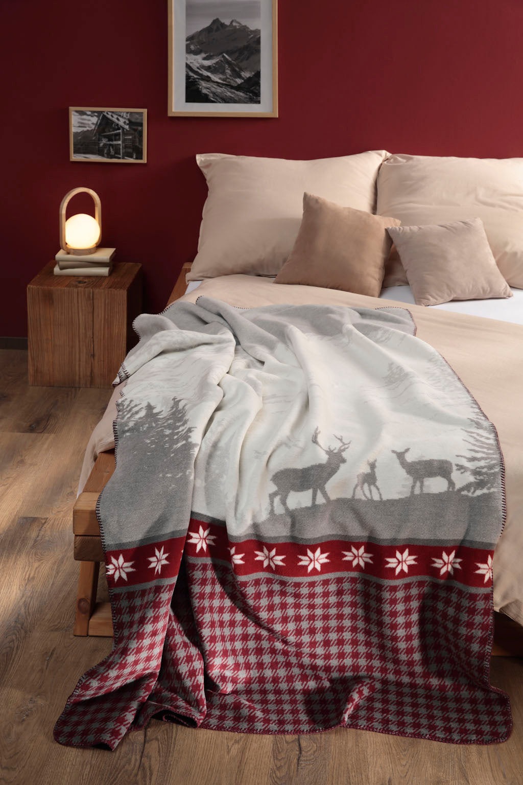 Alp View Blanket in cream, grey and red. Draped over a beige and white bed in a bedroom with wooden floor and red feature wall