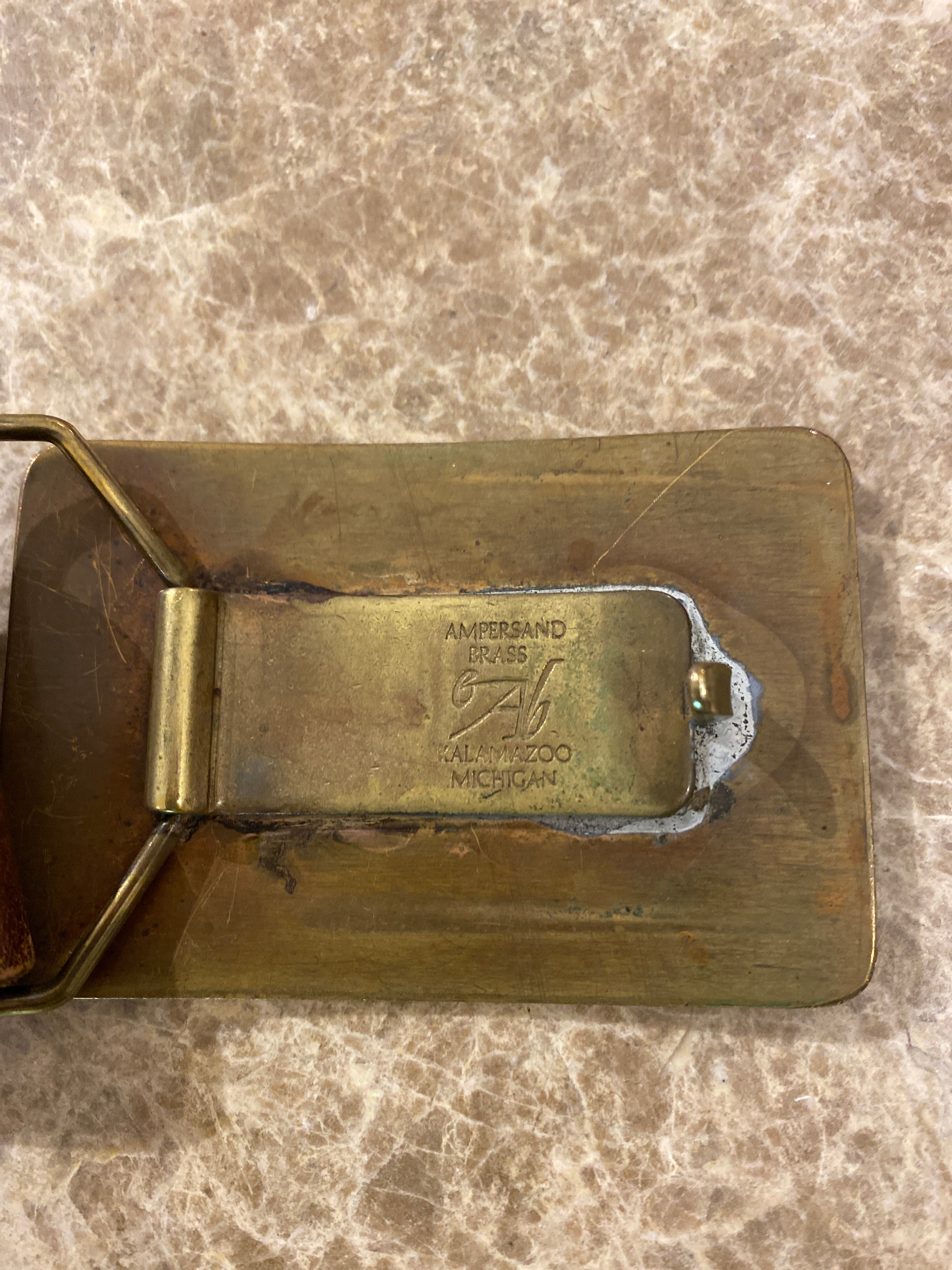 Vintage leather belt with an Ampersand Brass skier buckle. Close up of back of buckle,  shown on a brown & cream Ceasarstone bench