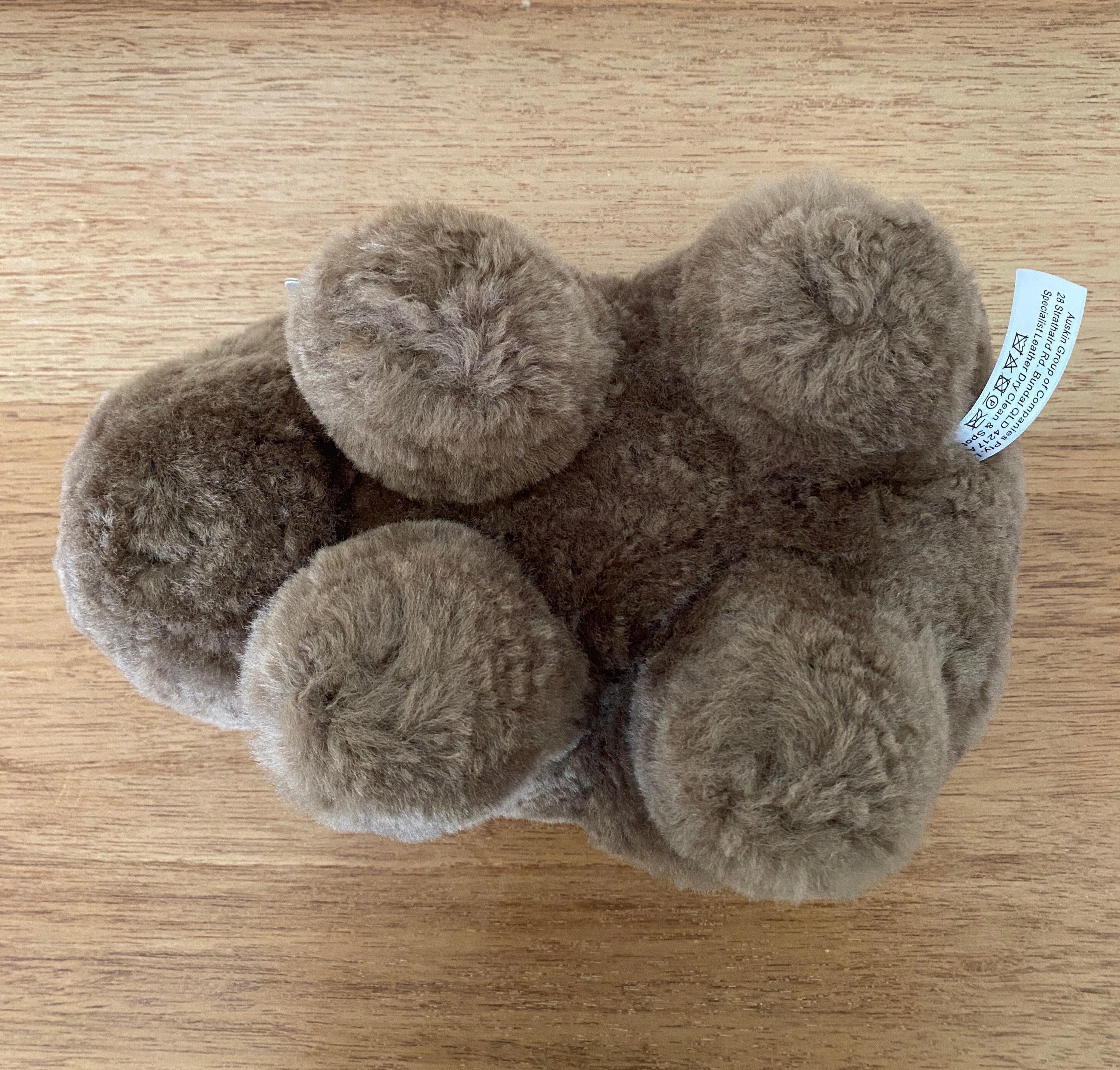 Winnie Wombat Sheepskin Soft Toy; shorn brown sheepskin with dark brown leather nose, plastic dark brown eyes and small brown leather inner ears and toes. Upside down view, on a wooden table.