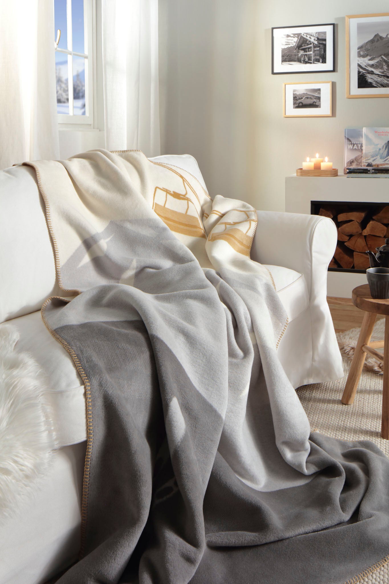 Mountain Valley Blanket in cream, grey and yellow. Draped over a white couch in a white & beige lounge room with wooden accents