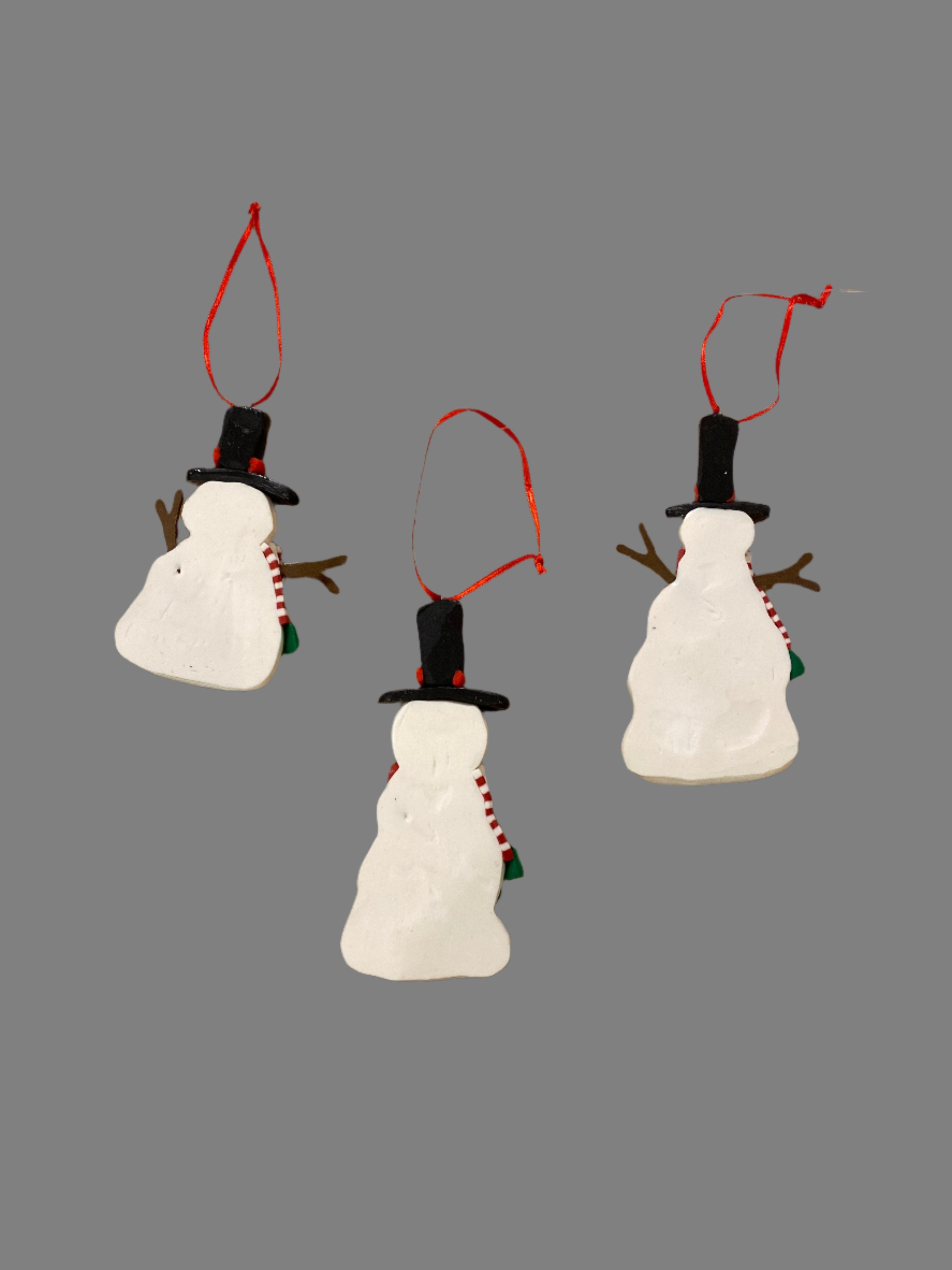 Set of 3 White snowman ornaments, wearing black hats with red hat bands, brown sticks for arms, a red &amp; white striped scarf with a green fringe, and with black dots down the chest and orange noses. Back of ornaments 