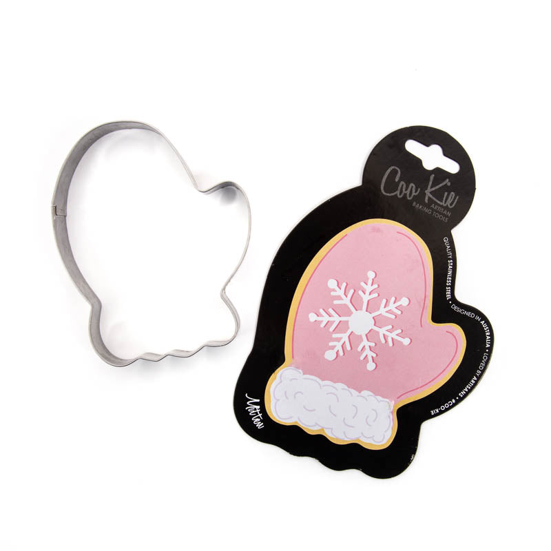 Image of mitten cookie cutter separated from its black cardboard backing depicting a pink mitten with a snowflake on it. Shown against a white backdrop. 