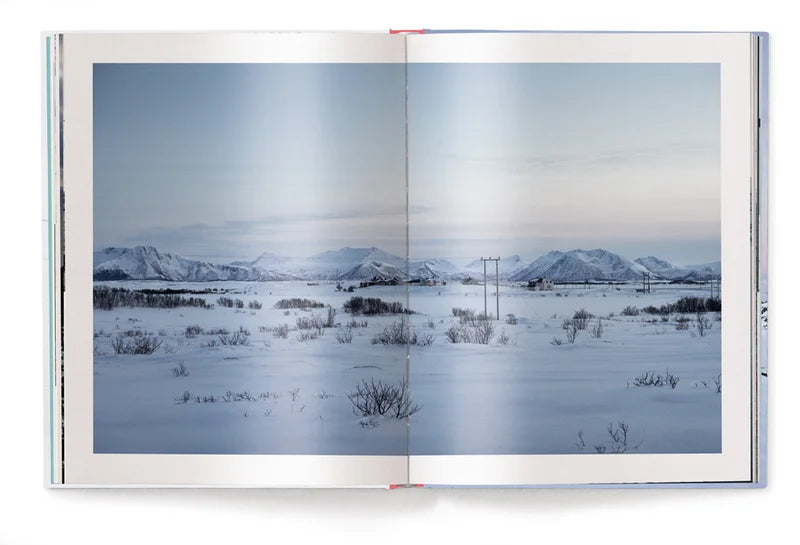 Image shows a page of the book, a photograph of a village in the distance. Flat snow covered land in the foreground before the landscape become mountainous