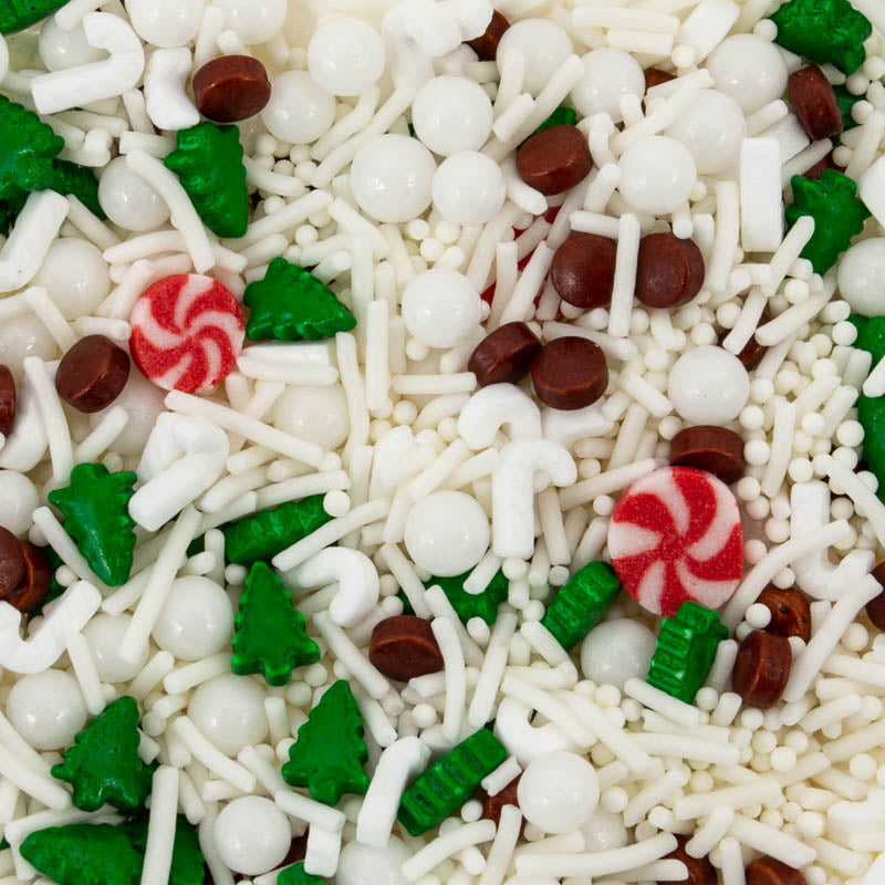Image of white snowflake, green tree, red & white candy, white ball and brown circular shaped sprinkles for cake or cookie decorating spread across a flat surface