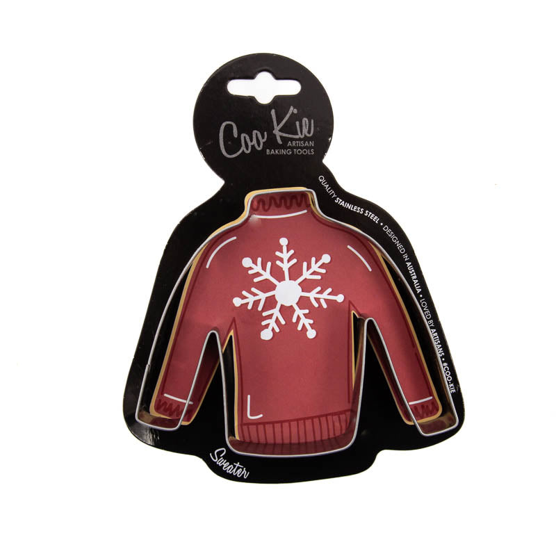 Image of jumper cookie cutter on a black cardboard depicting a red jumper with a snowflake on it. Shown against a white backdrop. 