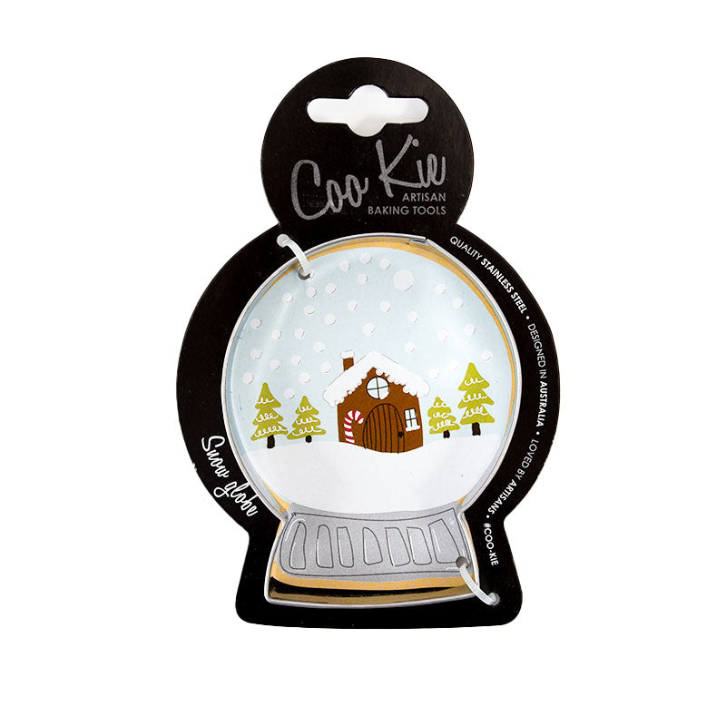 Image of a snow globe cookie cutter on a black cardboard depicting a snowglobe with snowy cabin scene within it. Shown against a white backdrop. 