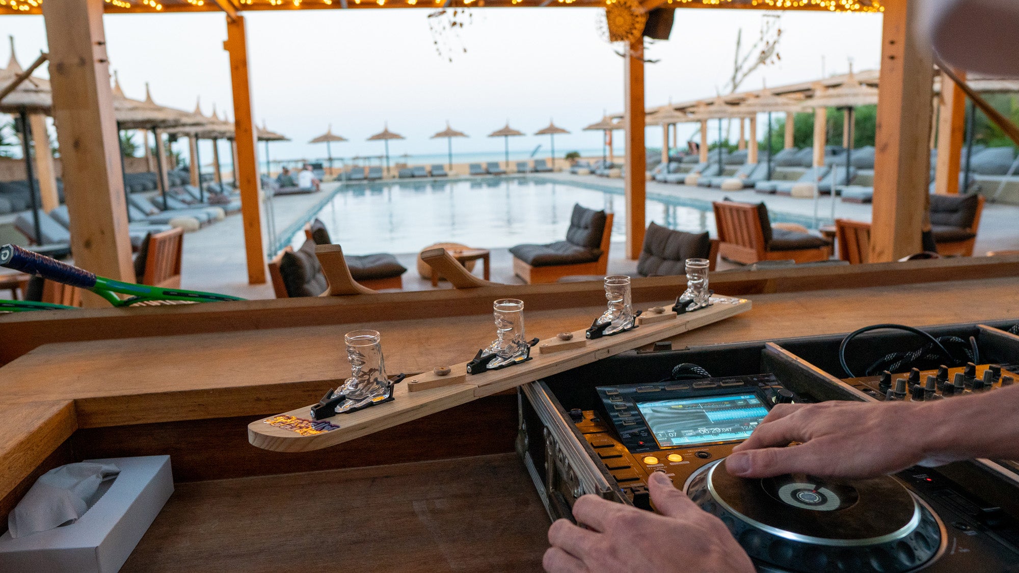 Photo of Apres Allstar SwigSki3000 a modular wooden ski that comes in 4 parts and clicks together to make a single shot ski. Image is of the ShotSki3000 in a DJ booth in front of a swimming pool.