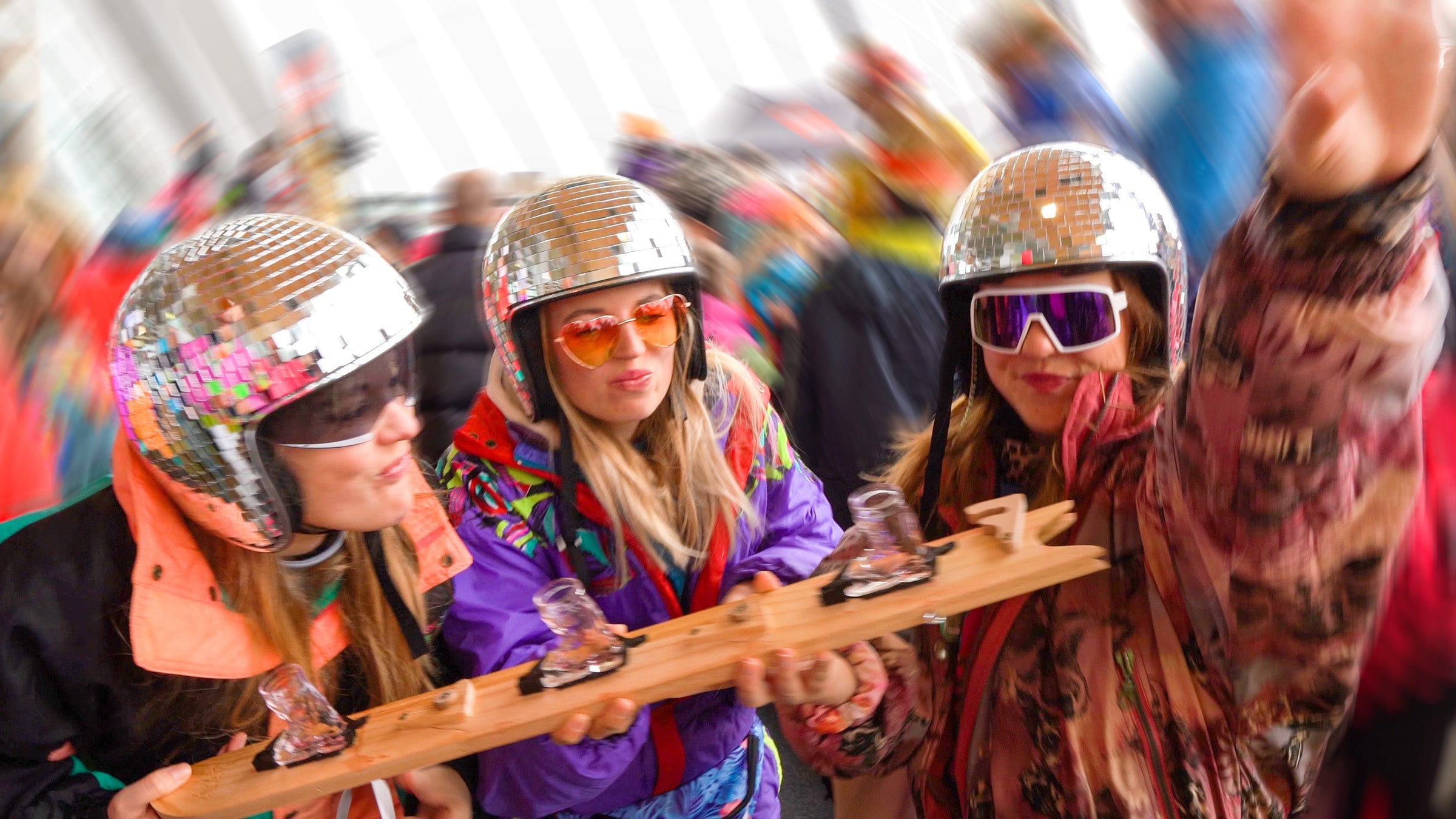 Party girls wearing colourful vintage ski gear and mirror helmets, holding a SwigSki300