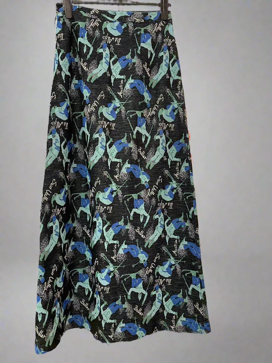 "Mt Buller" A-line full length skirt with side zip. Size 14 (more like modern day 8-10). Pattern is teal and blue skiers on a black background with the words Buller, Sun Valley, The Alps, Austria printed in white. Back
