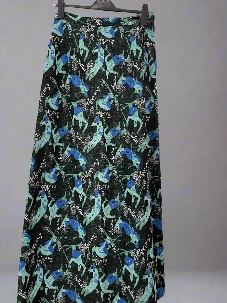 "Mt Buller" A-line full length skirt with side zip. Size 14 (more like modern day 8-10). Pattern is teal and blue skiers on a black background with the words Buller, Sun Valley, The Alps, Austria printed in white. Front 2