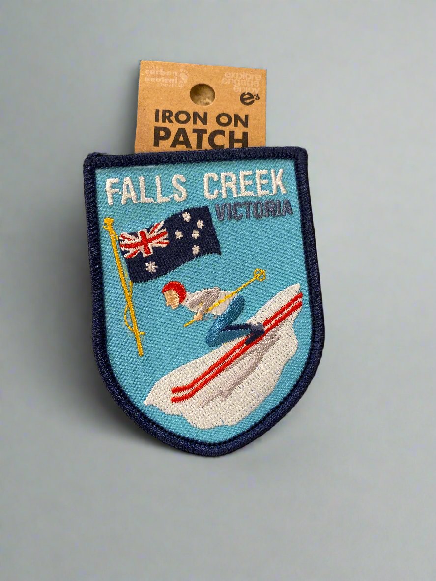 Retro Vintage Style Falls Creek Embroidery Iron On Patch. Skier with red hat, white & grey top, blue pants, black boots, yellow poles & red skis on a sky blue background with Australian Flag