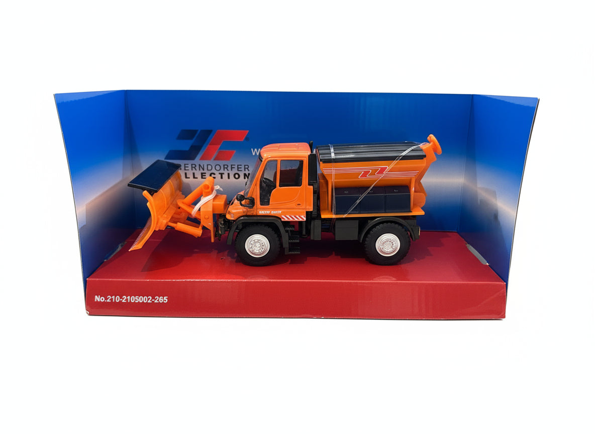 This image shows the Jaegerndorfer Snow Clearing Truck with straight plow attachment from the side, in part of it's blue and red box on a white background. 