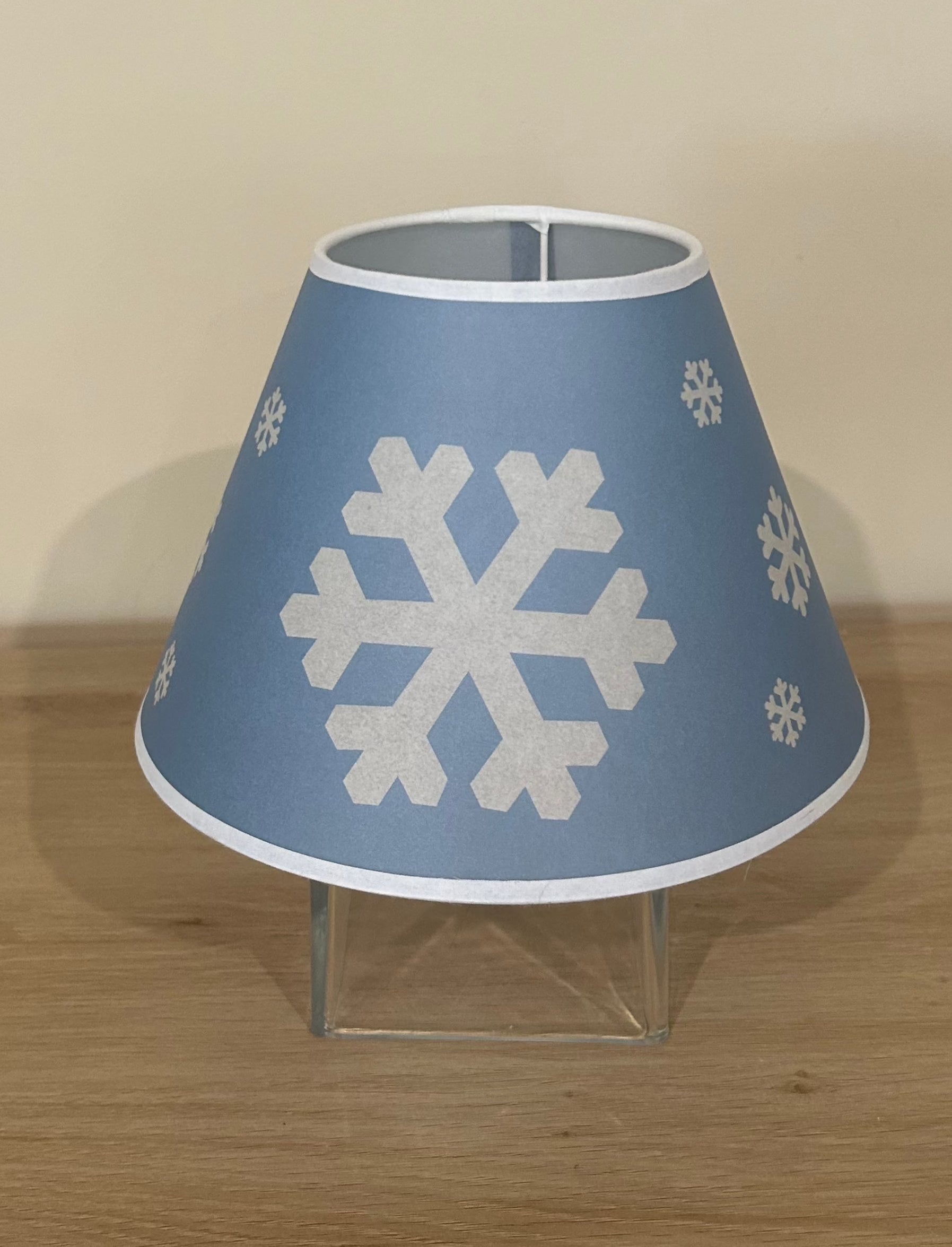 La Maison De Gaspard lamp shade with a snowflake printed canvas lamp shade in blue and white. On wooden table, resting on glass cube