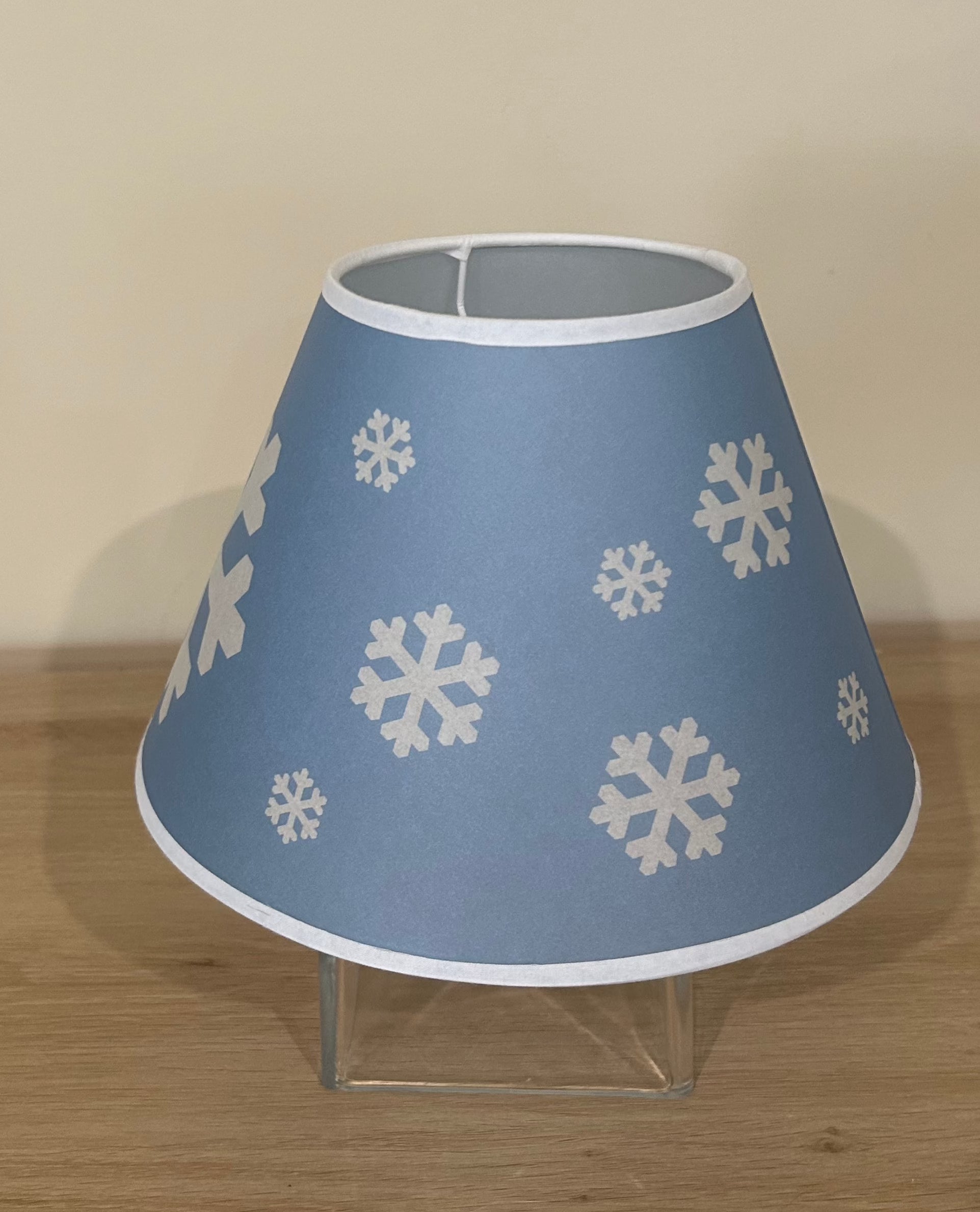 La Maison De Gaspard lamp shade with a snowflake printed canvas lamp shade in blue and white. On wooden table, resting on glass cube. Alternate angle