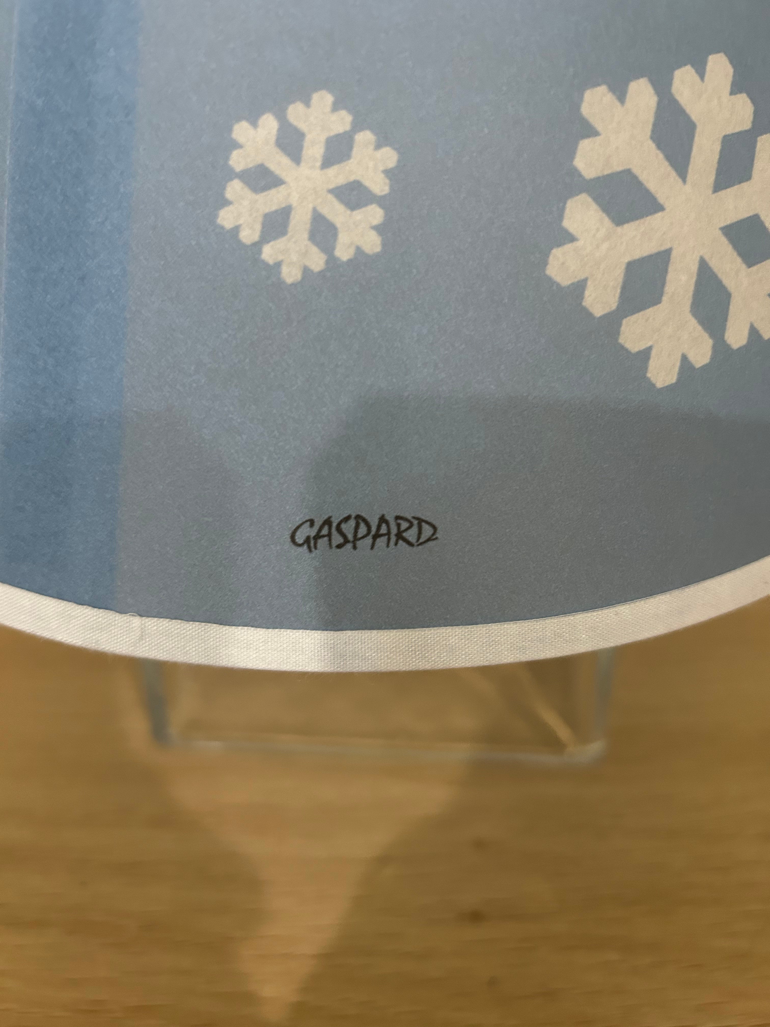 La Maison De Gaspard lamp shade with a snowflake printed canvas lamp shade in blue and white. On wooden table, resting on glass cube. Close up of signature