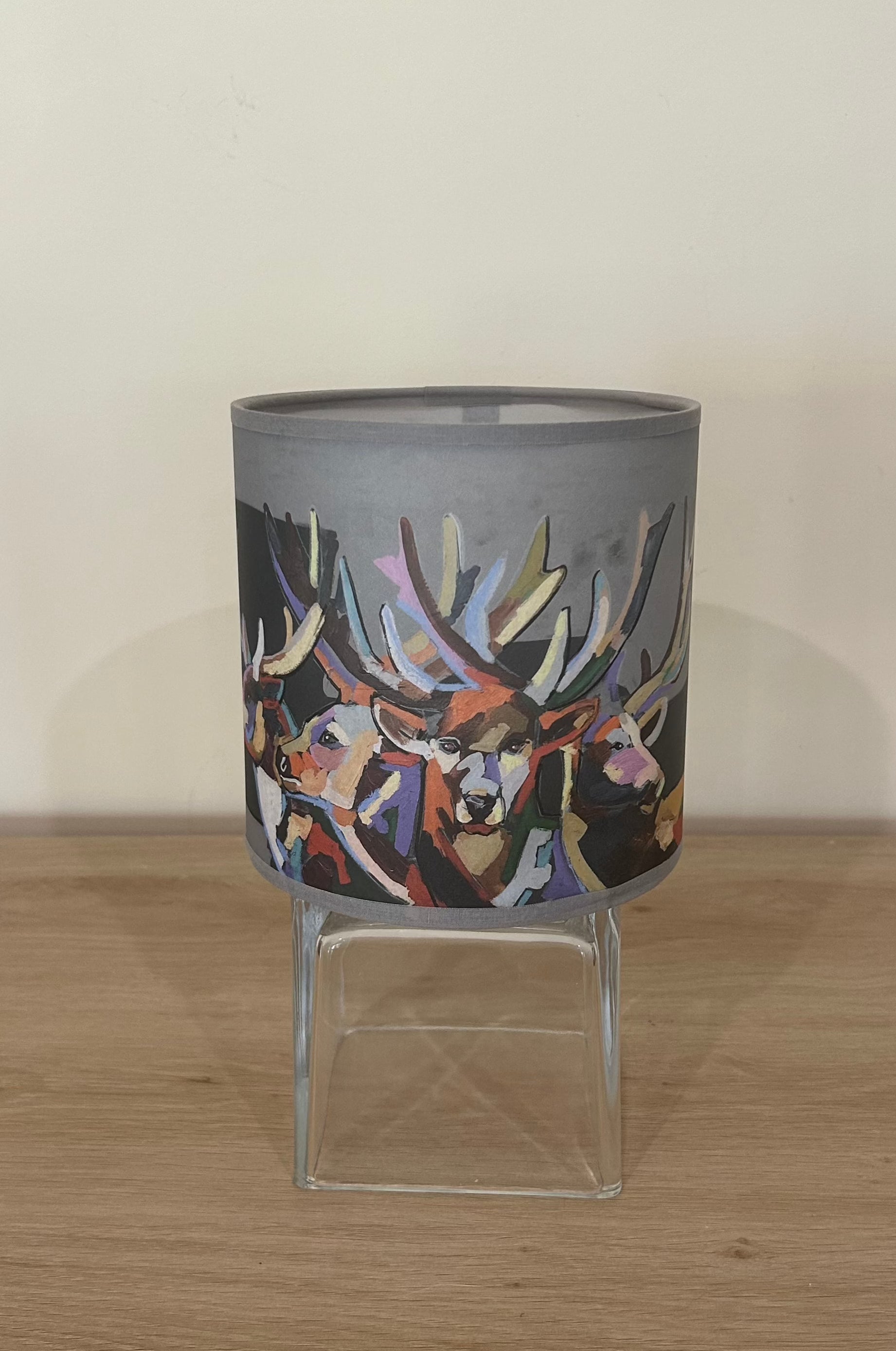 La Maison De Gaspard colourful lamp shade with deers rendered gorgeously in multiple colours. On a wooden table resting on a glass cube