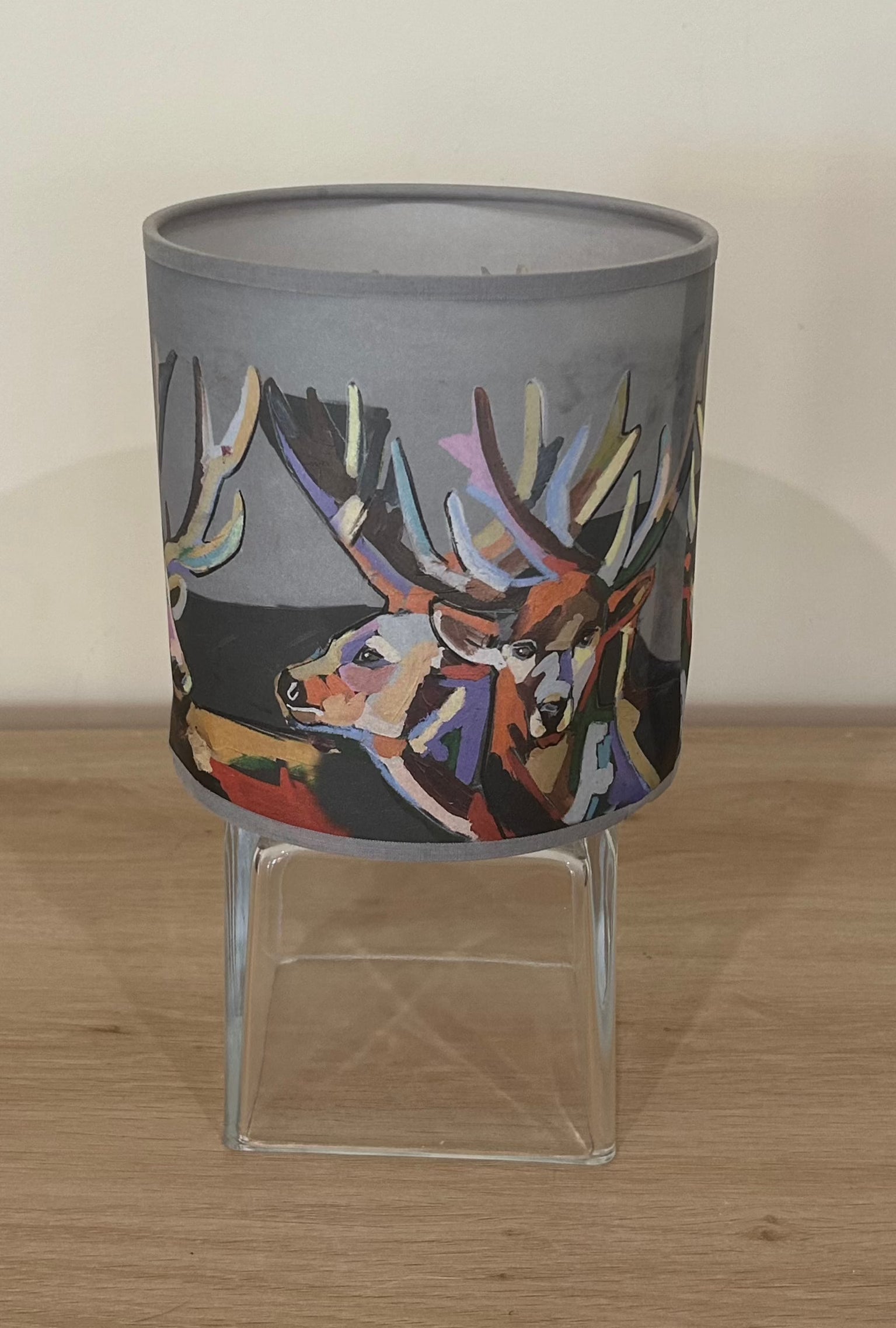 La Maison De Gaspard colourful lamp shade with deers rendered gorgeously in multiple colours. On a wooden table resting on a glass cube. Alternate angle