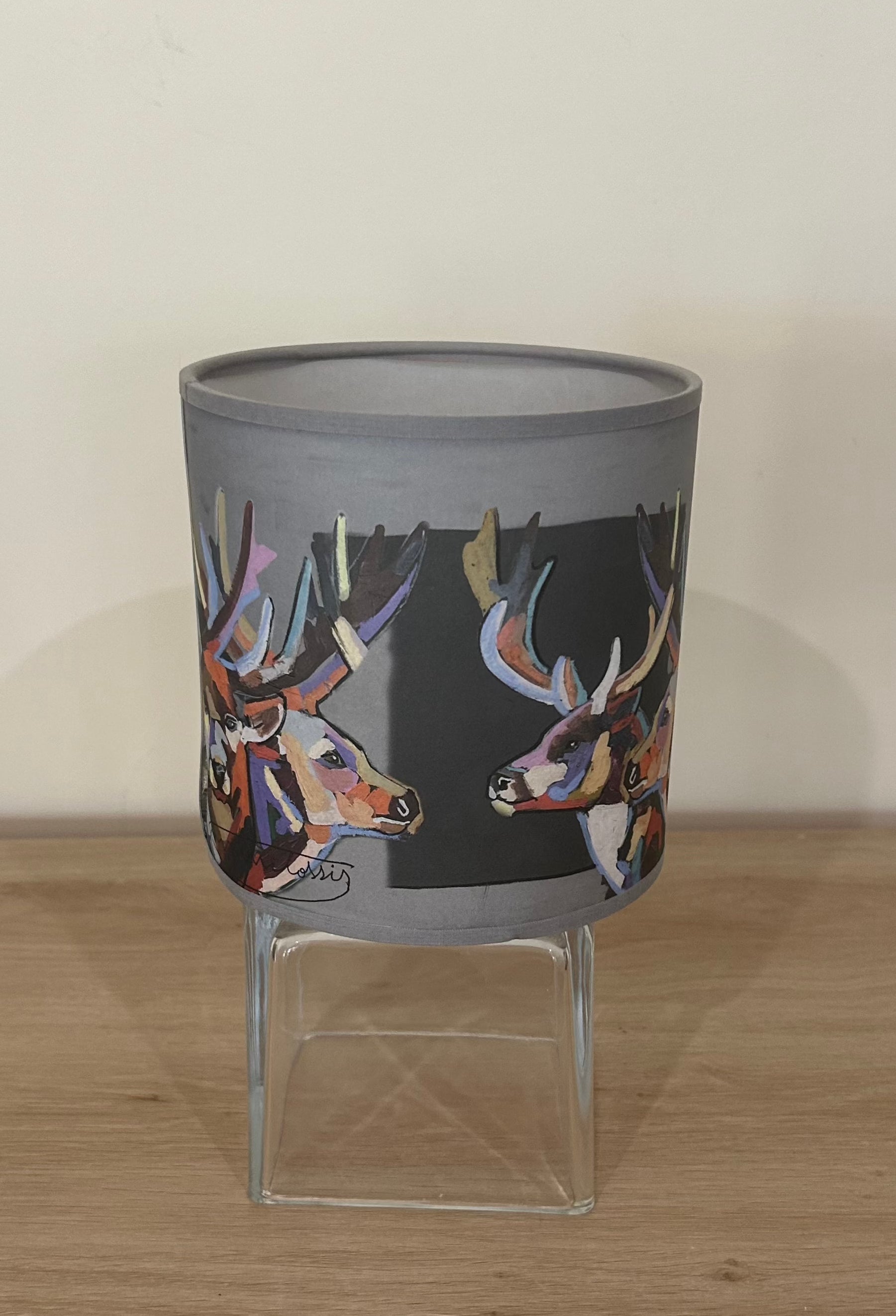 La Maison De Gaspard colourful lamp shade with deers rendered gorgeously in multiple colours. On a wooden table resting on a glass cube. Different angle