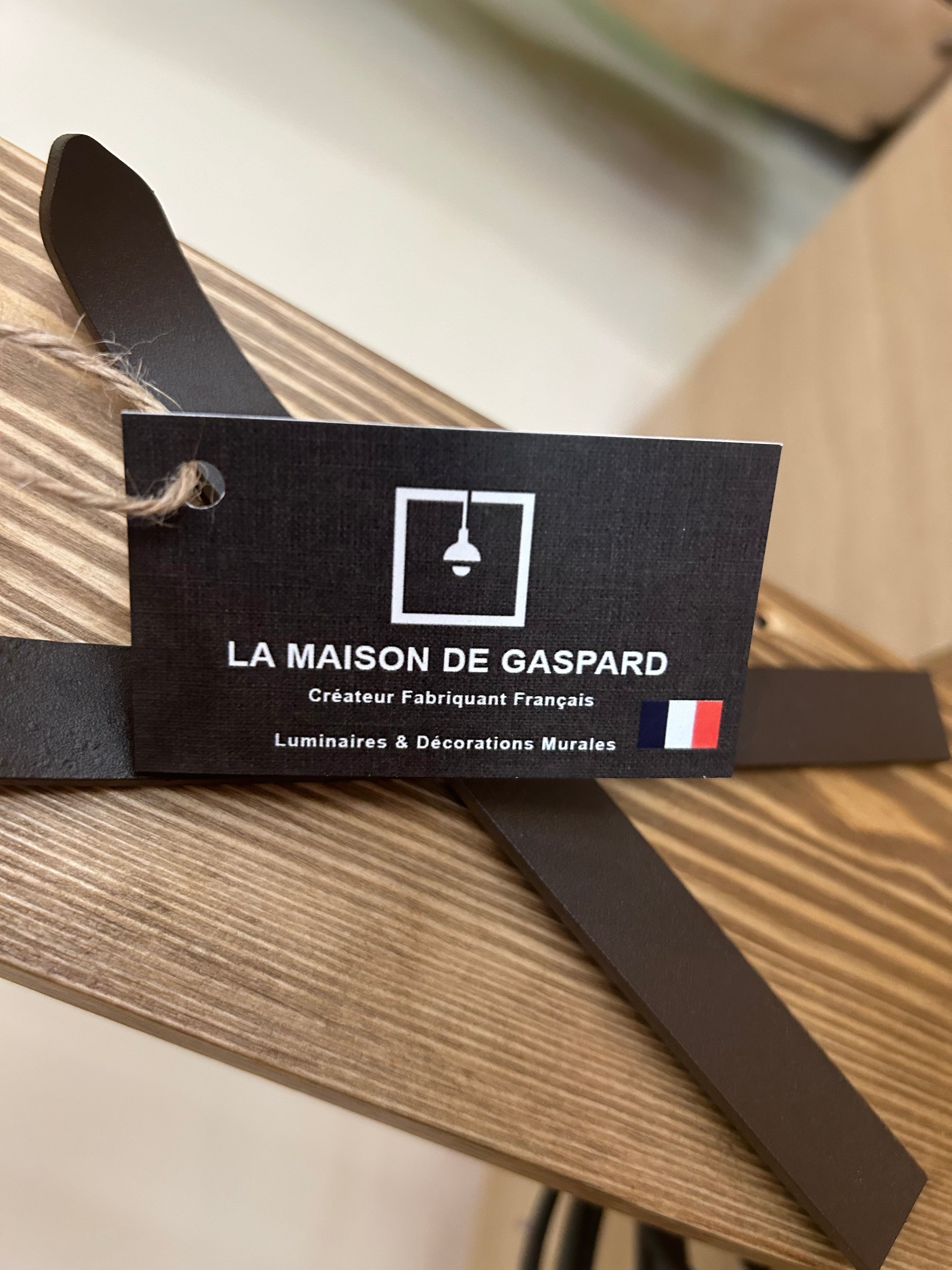 La Maison De Gaspard: a square solid wooden base and stem to which a pair of metal skis is attached, from which a brown metal rod extend curving upwards attached to a pair of metal poles that will hold up the lamp shade. On a wooden table