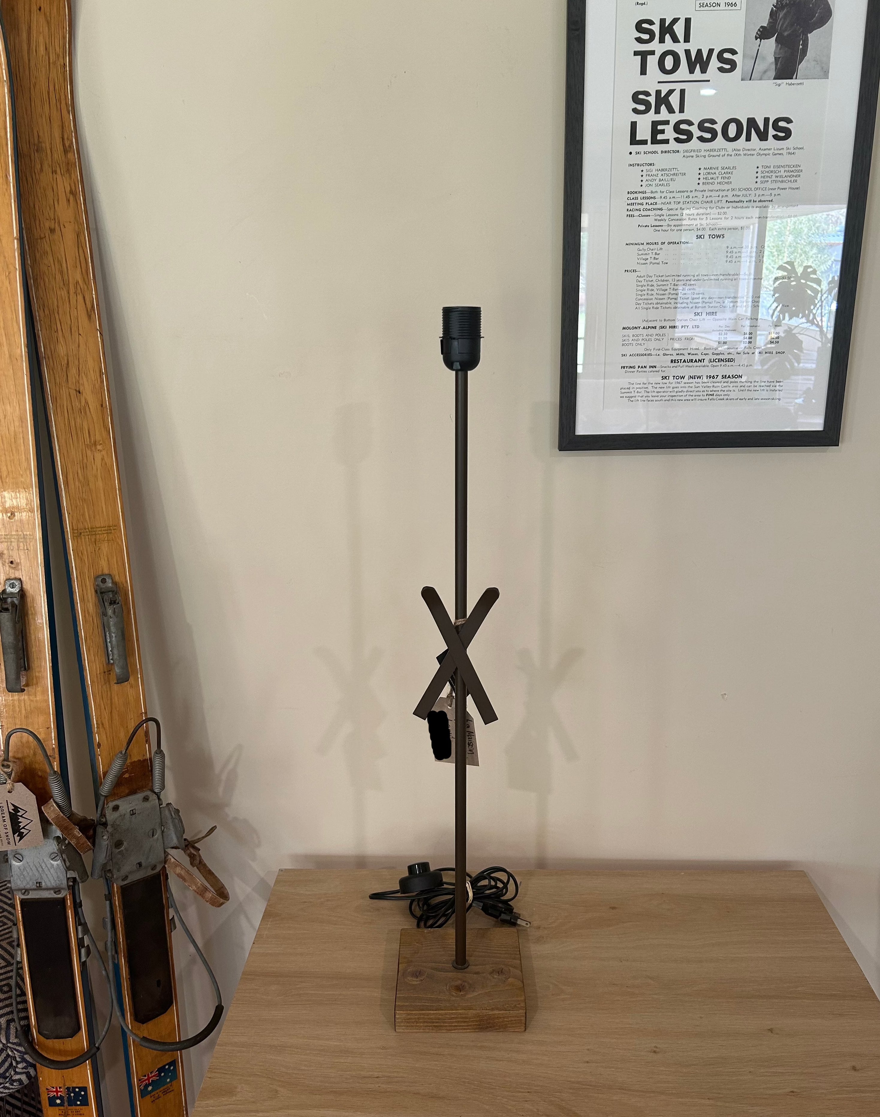 La Maison De Gaspard: a square solid wood base supporting a brown metal rod with crossed metal skis mid way up the rod. On a wooden table.