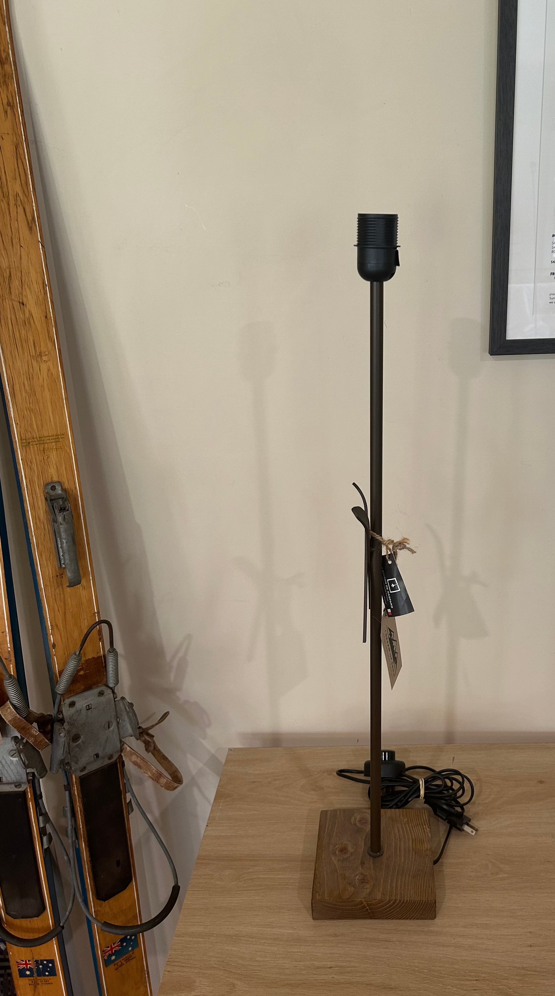 La Maison De Gaspard: a square solid wood base supporting a brown metal rod with crossed metal skis mid way up the rod. On a wooden table. alternate angle