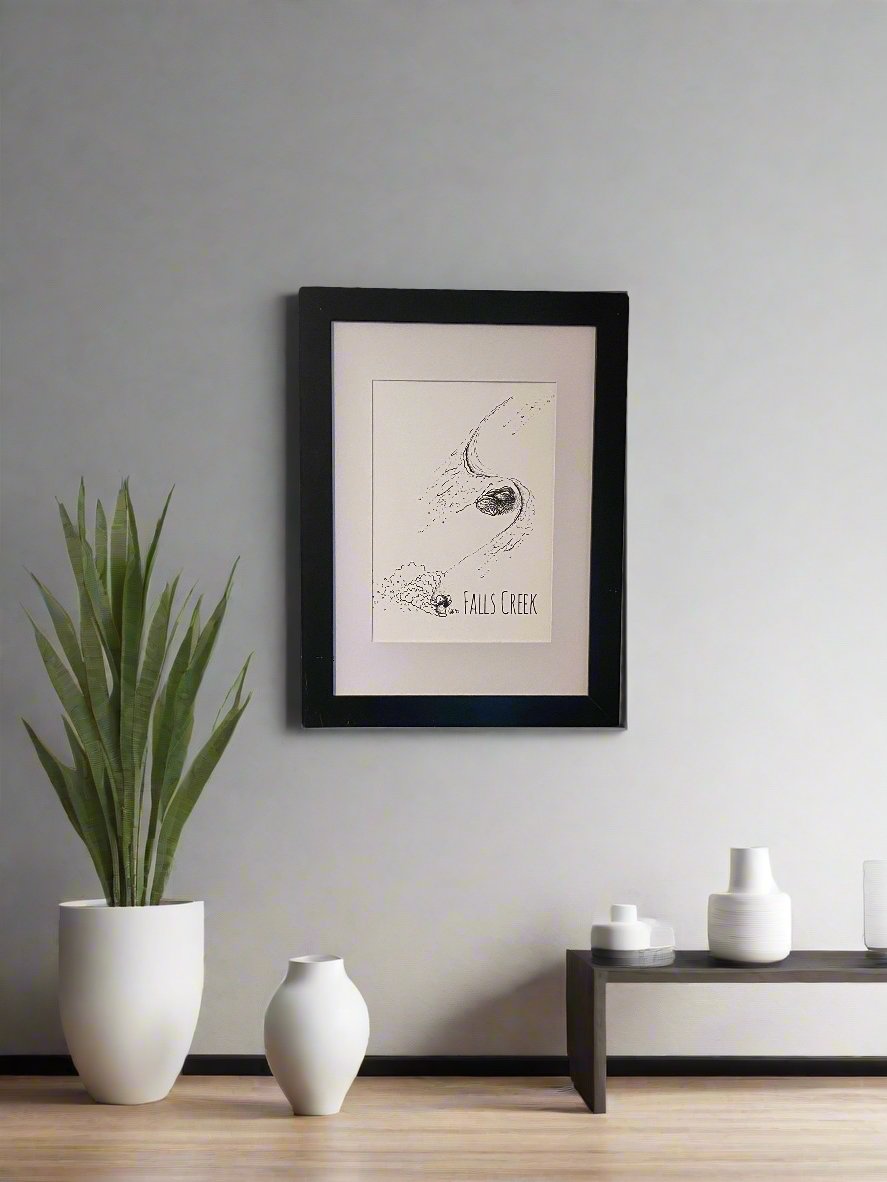 Print of a snowboarding koala turning around snow gum trees, with the words Falls Creek printed underneath the image, shown in a thick black frame.