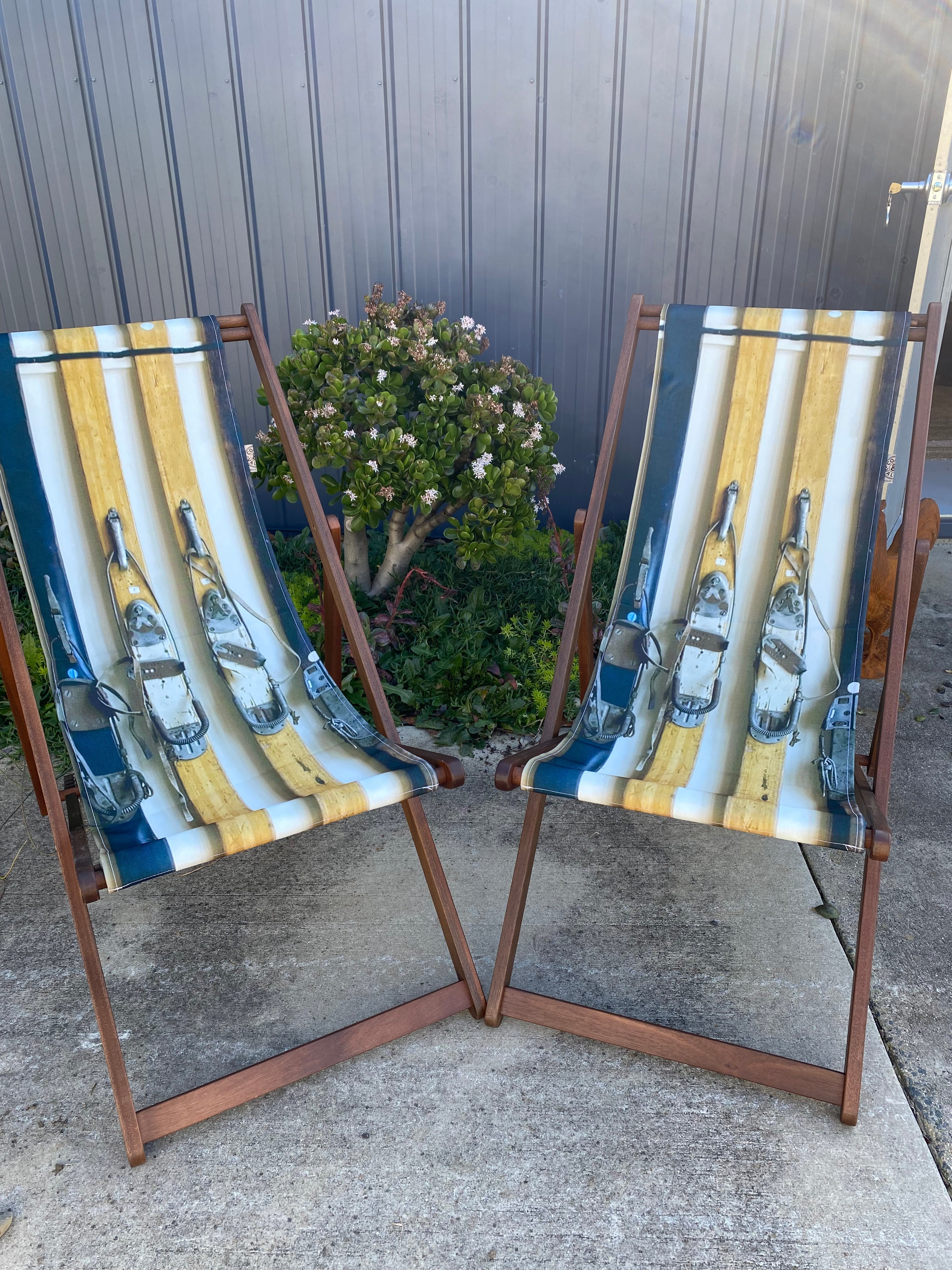 Pair of Coast & Valley Deck Chairs: Vintage Ski design showing 2 pairs of vintage wooden skis with bindings. 2 chairs facing forward. On a concrete floor against a blue steel shed and door with garden bed in the background