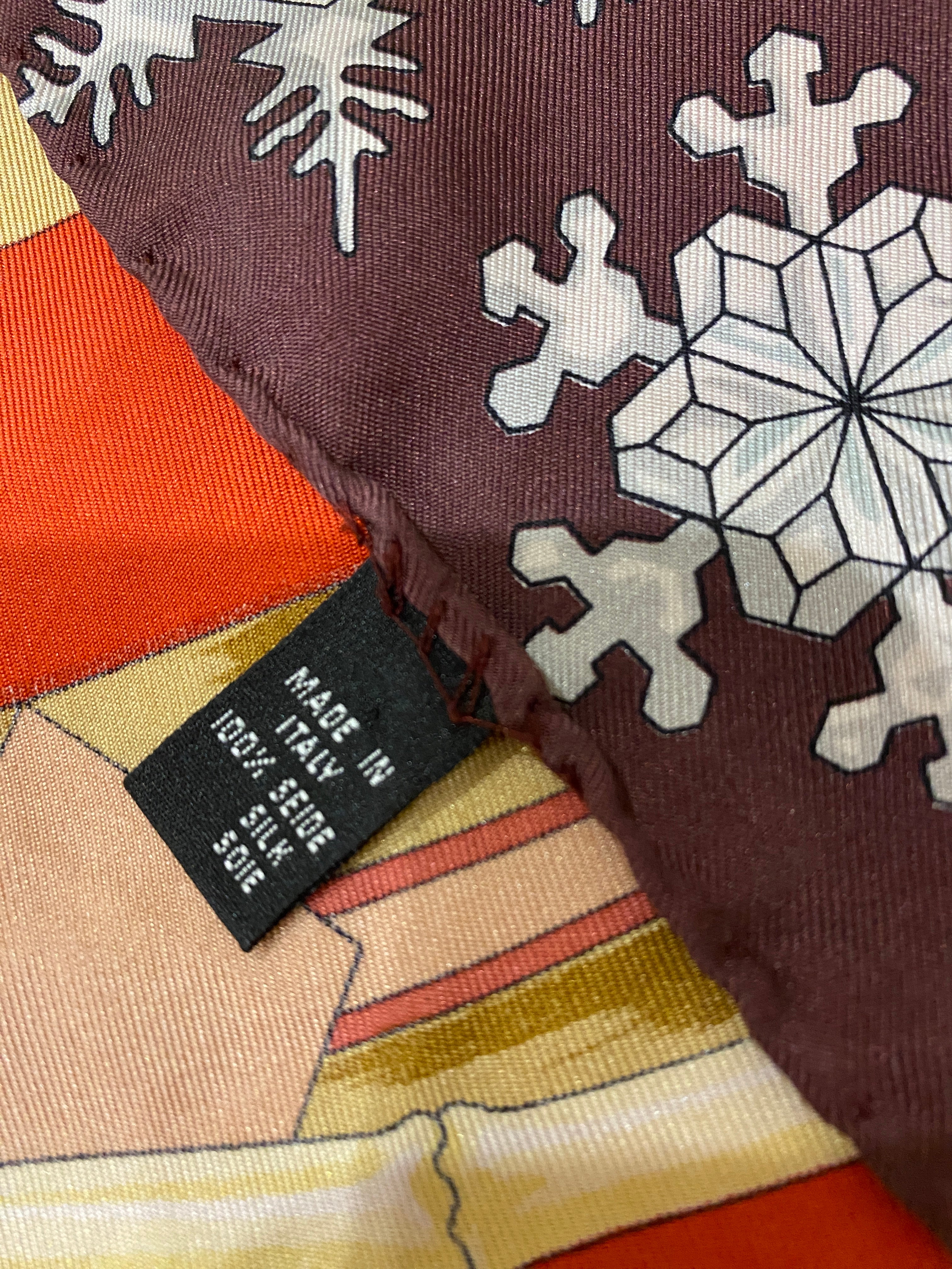 Bogner Silk Vintage Ski Scarf in red, brown white and beige. Snowflakes border the scarf, with the central square illustrating wooden skis and poles. Made in Italy, 100% Silk label. Shown against wooden background