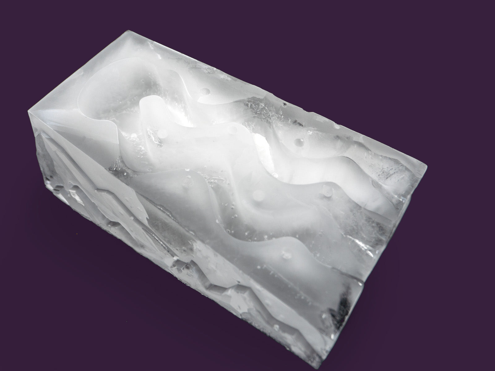 Photo of the ice shot slope slalom, with 2 funnels within the ice through which liquor is poured to chill it. The image is set against a purple backdrop. The ice is viewed from the front right on an angle.