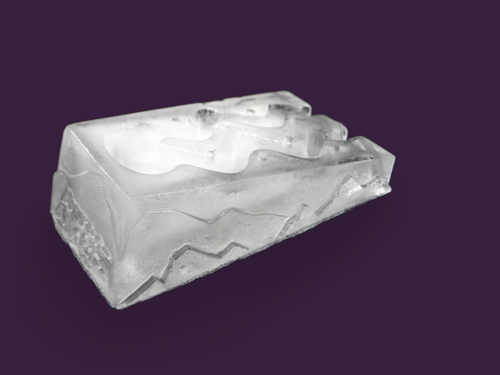 Photo of the ice shot slope slalom, with 2 funnels within the ice through which liquor is poured to chill it. The image is set against a purple backdrop. The ice is viewed from the rear right hand side on an angle.