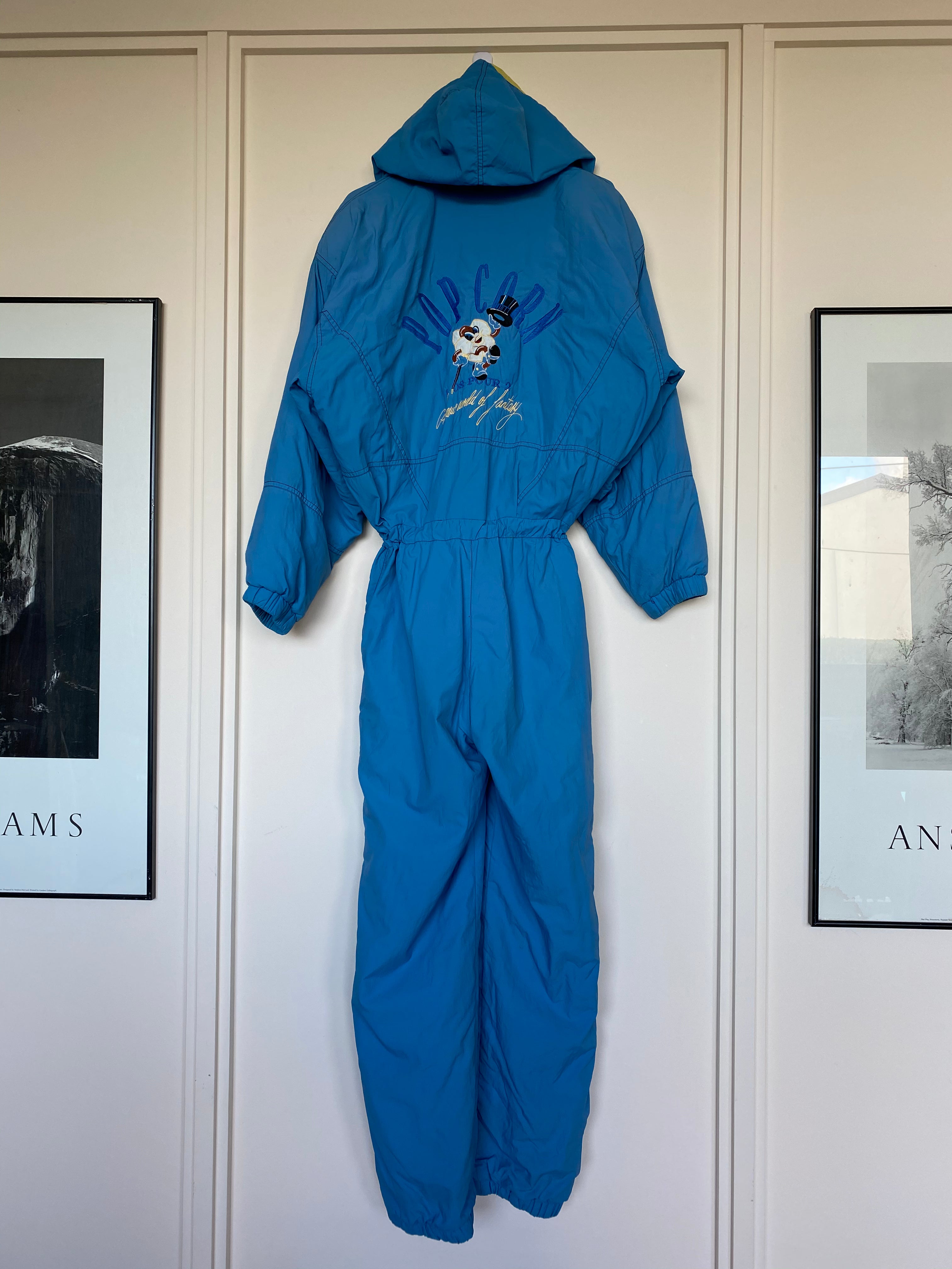 Vintage cornflower blue, with yellow and orange stripe "10S Pour 2" 1-piece snow suit with embroidery "Popcorn 10s Pour 2, A New World of Fantasy" on back shoulder and front right hand chest. Back