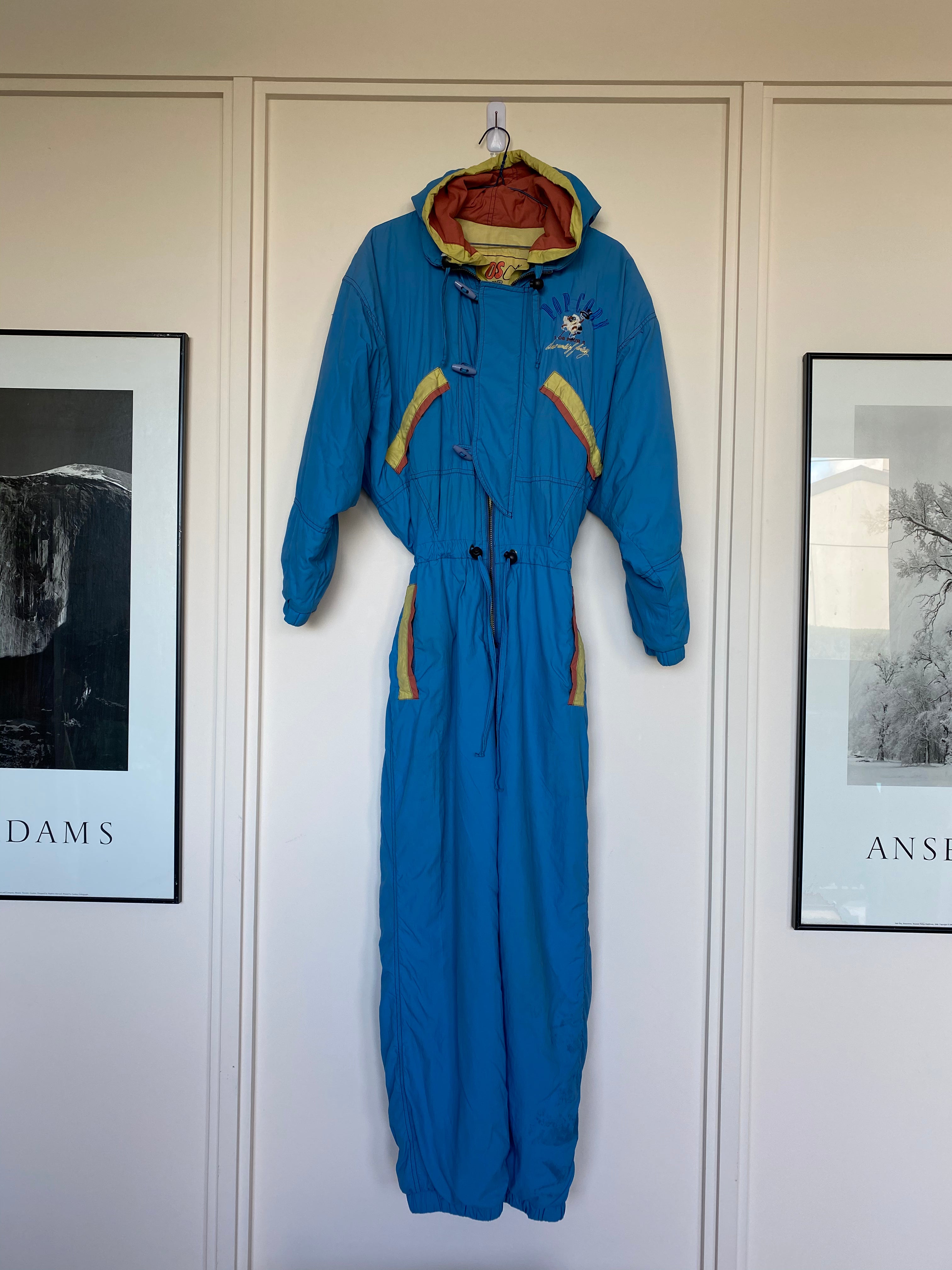 Vintage cornflower blue, with yellow and orange stripe "10S Pour 2" 1-piece snow suit with embroidery "Popcorn 10s Pour 2, A New World of Fantasy" on back shoulder and front right hand chest. Front