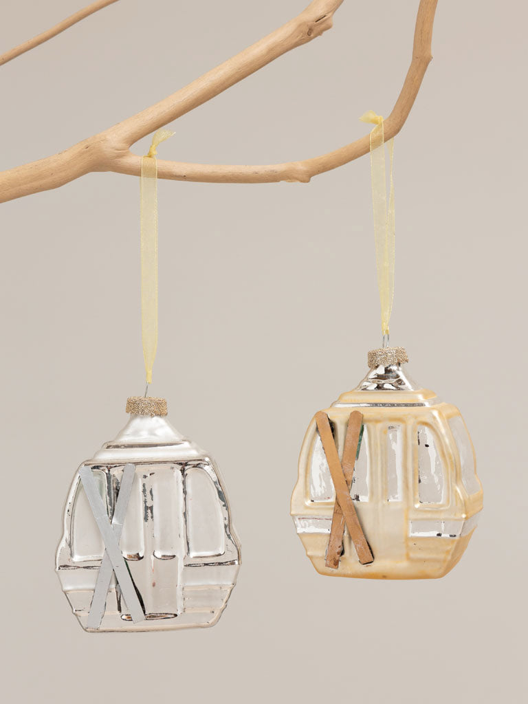 Pair of Gold and silver gondolas hanging from a branch against a pale background