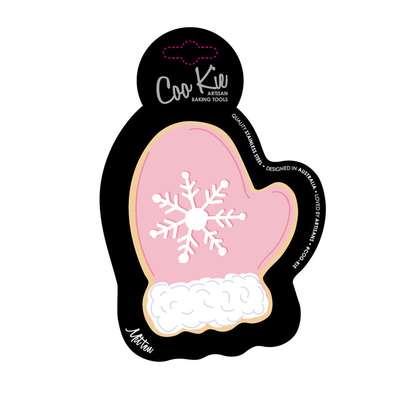 Image of mitten cookie cutter on a black cardboard depicting a pink mitten with a snowflake on it. Shown against a white backdrop. 