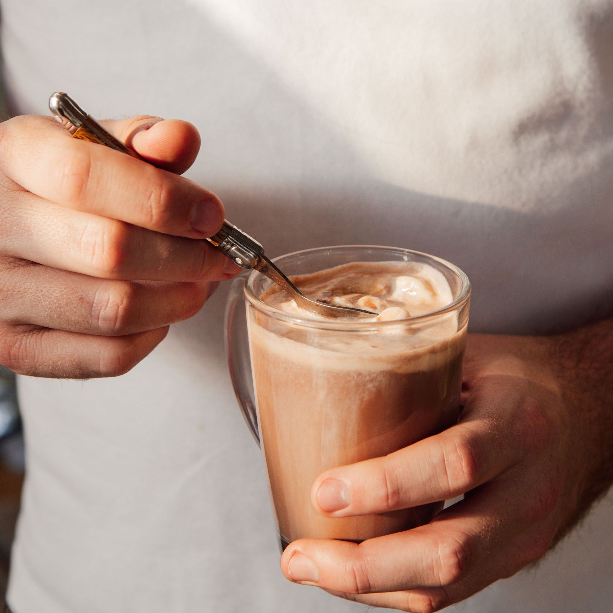Photo of a person weraing a white t-shirt holding a mug of Gewürzhaus Feel Good Hot Chocolate . Shown against a light  background.
