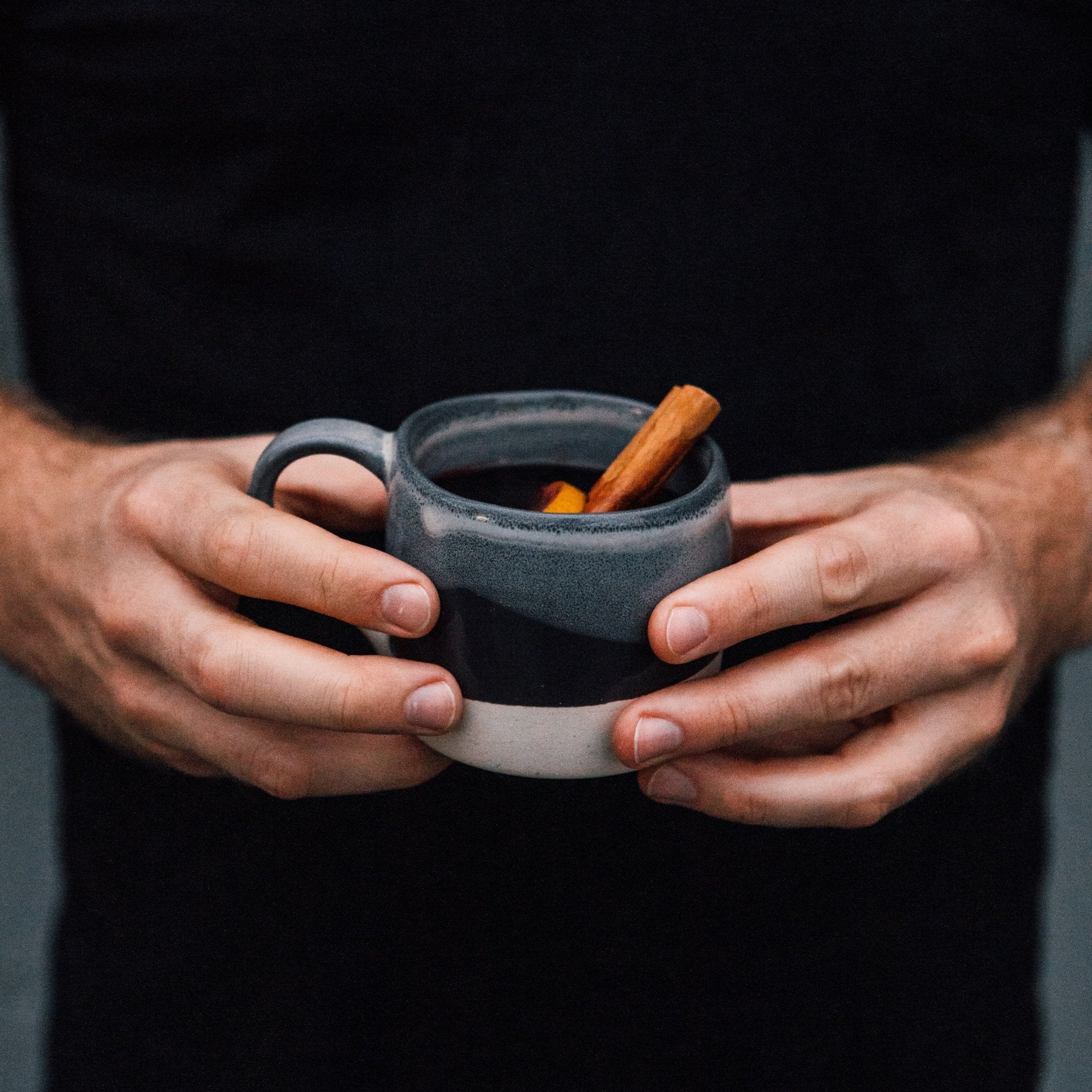 Photo of a person weraing a black t-shirt holding a mug of Gewürzhaus Glühwein . Shown against a light blue background.