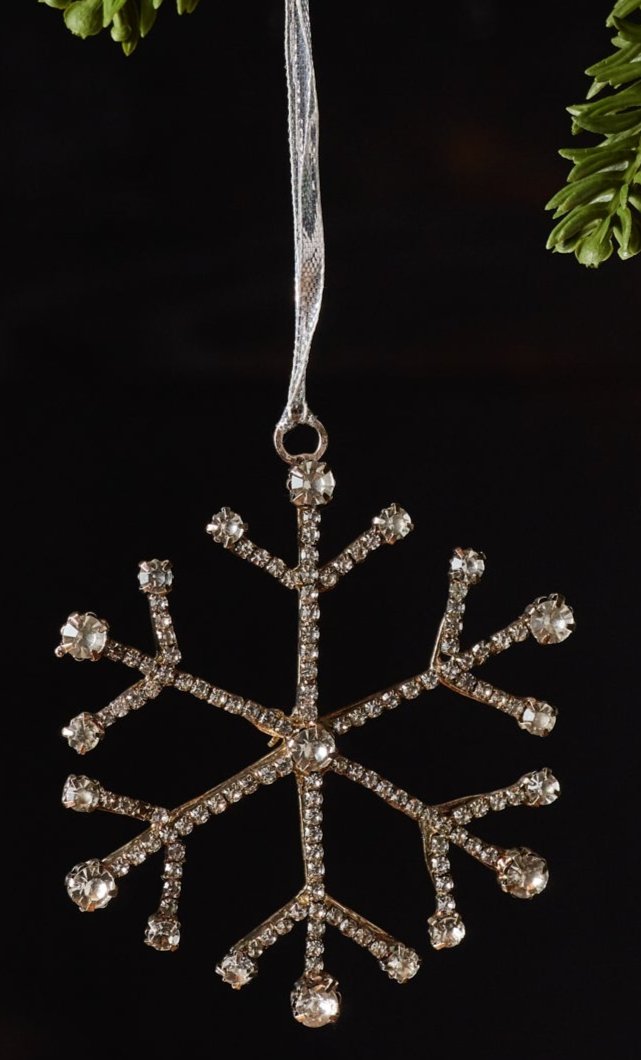 A Jewel Snowflake steel and glass hanging ornaments hanging from Christmas tree branches against a dark background