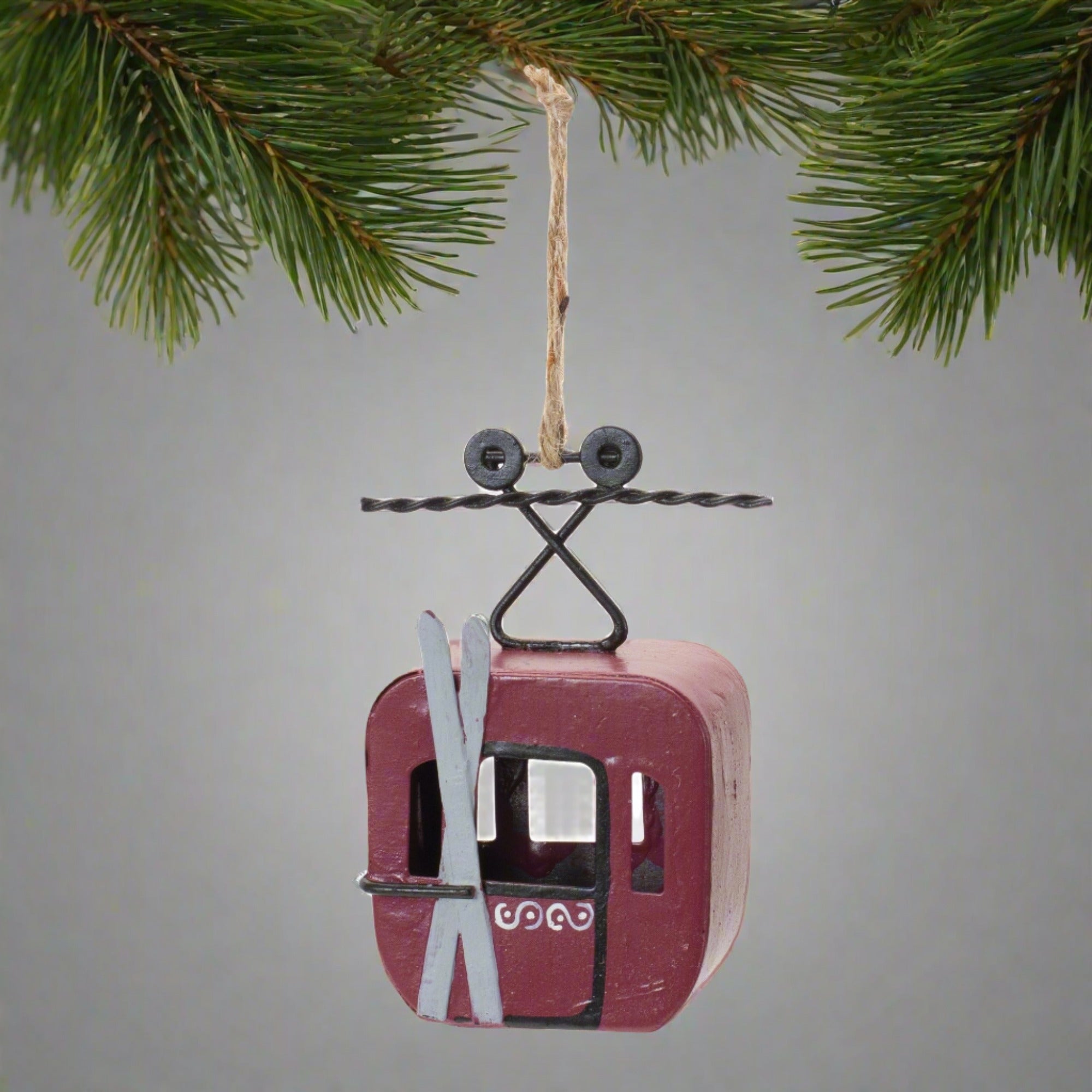 Red metal gondola with skis on outside hung from a fir tree branch