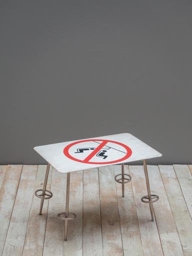 Small 'no swinging the chair' sign side table, with four legs shaped as ski poles, on wooden floor against a grey wall