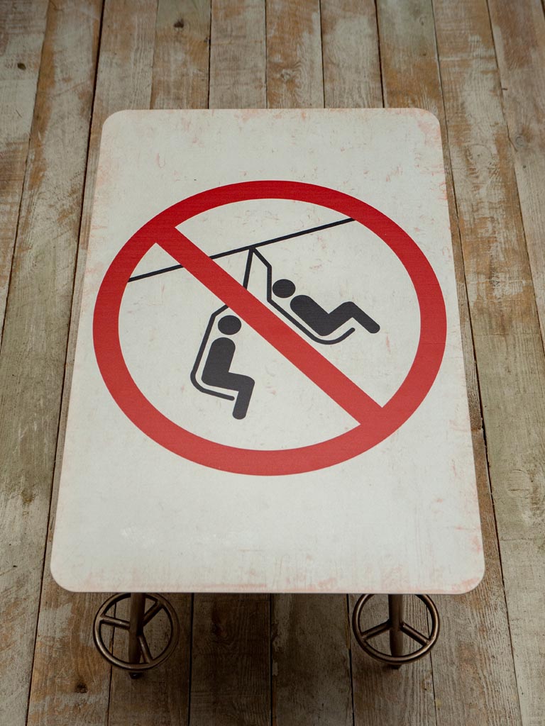 Small 'no swinging the chair' sign side table viewed from above, with four legs shaped as ski poles, on wooden floor against a grey wall