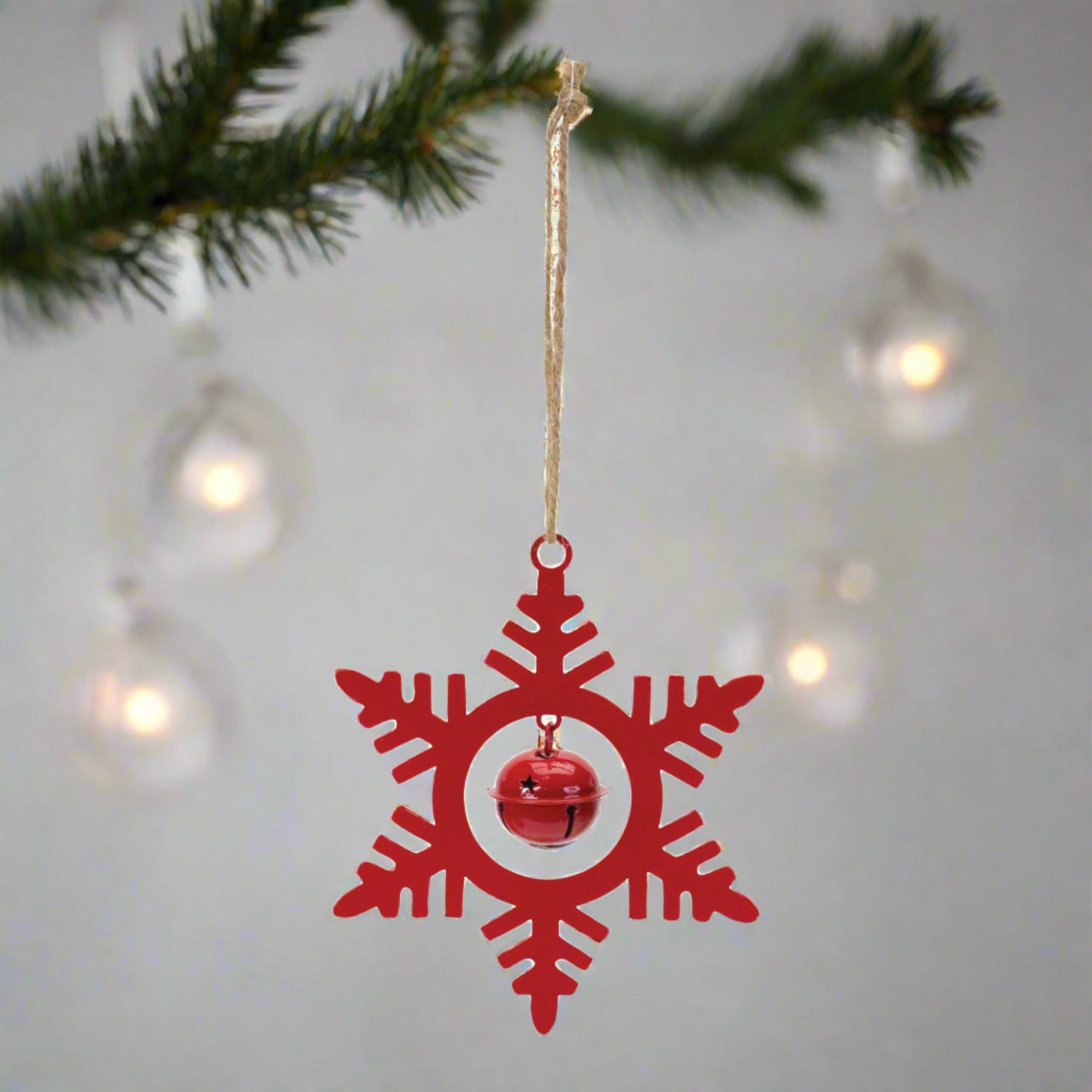 Red metal snowflake hanging ornament with a bell, hanging on a Christmas tree. 