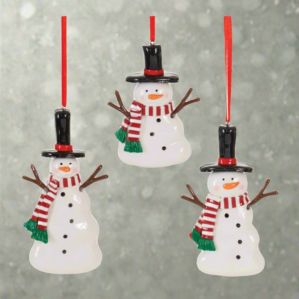 Set of 3 White snowman ornaments, wearing black hats with red hat bands, brown sticks for arms, a red &amp; white striped scarf with a green fringe, and with black dots down the chest and orange noses, against an icy background. 