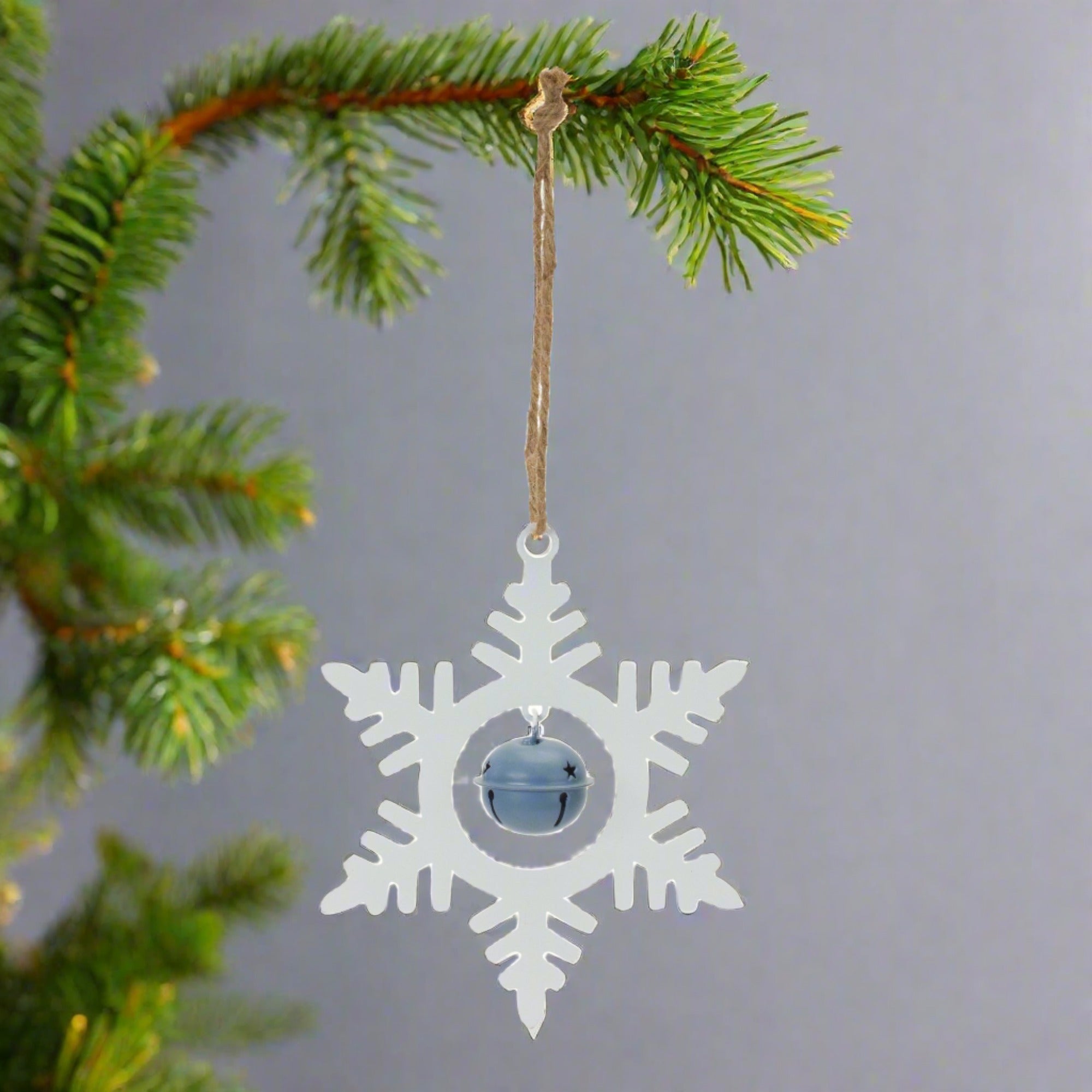 White metal snowflake hanging ornament with a blue bell, hanging on a Christmas tree. 