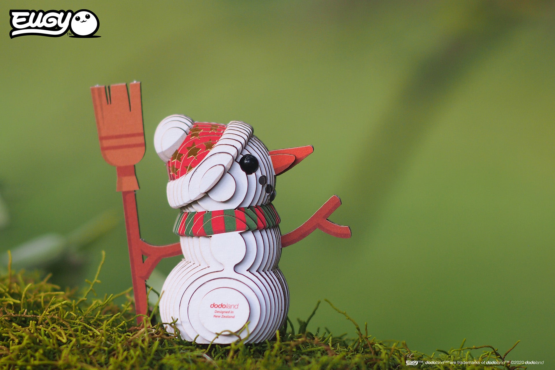 Image of an EUGY Snowman, facing right but viewed from the front & sitting on moss in front of a blurred green background