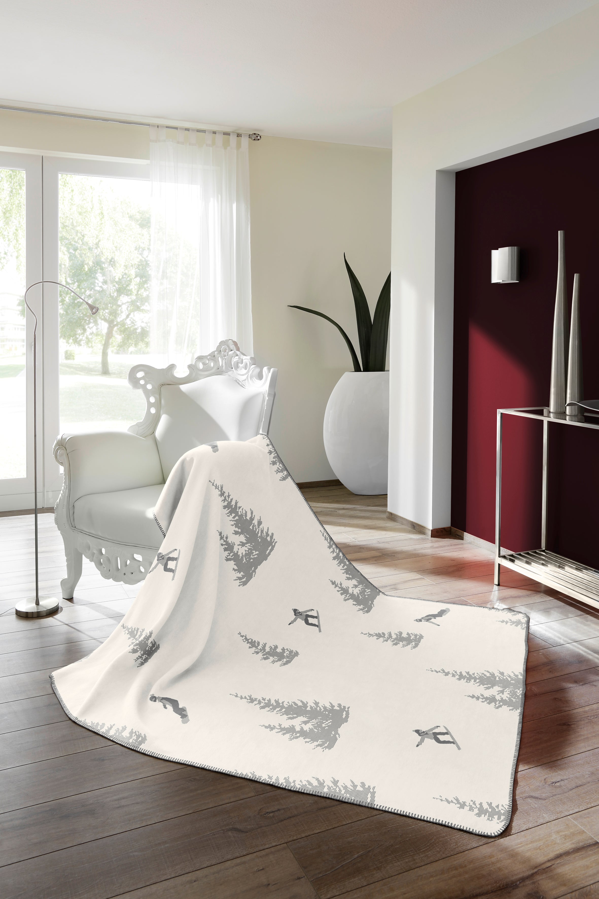 Snowboarding blanket - white side with grey snowboarders & trees shown draped across a white chair and timber floor in a lounge room.