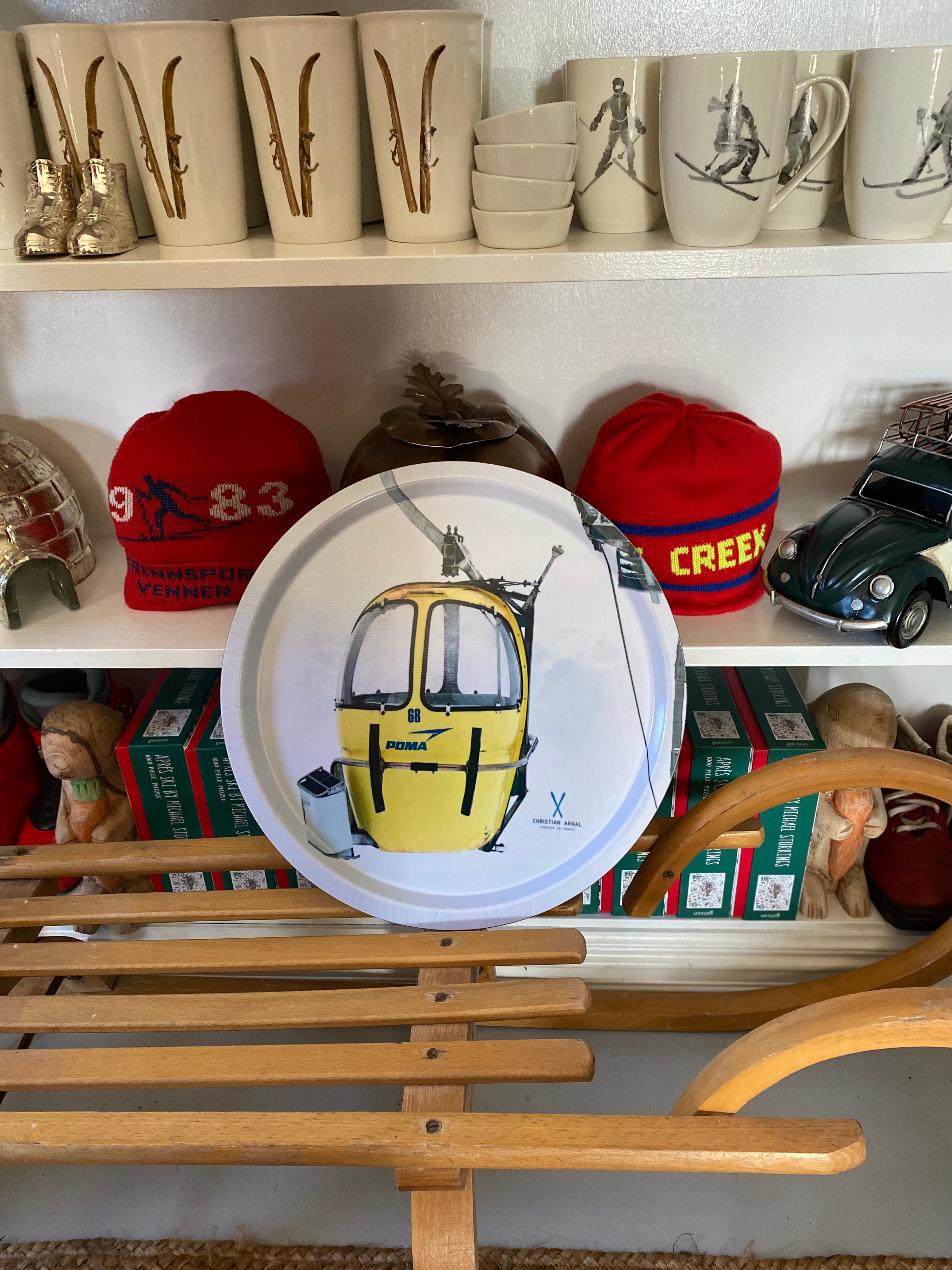Photo of a Yellow Vintage Gondola printed onto a Round White Serving Tray, resting on a vintage wooden sled in front of a white bookshelf filled with snow related products