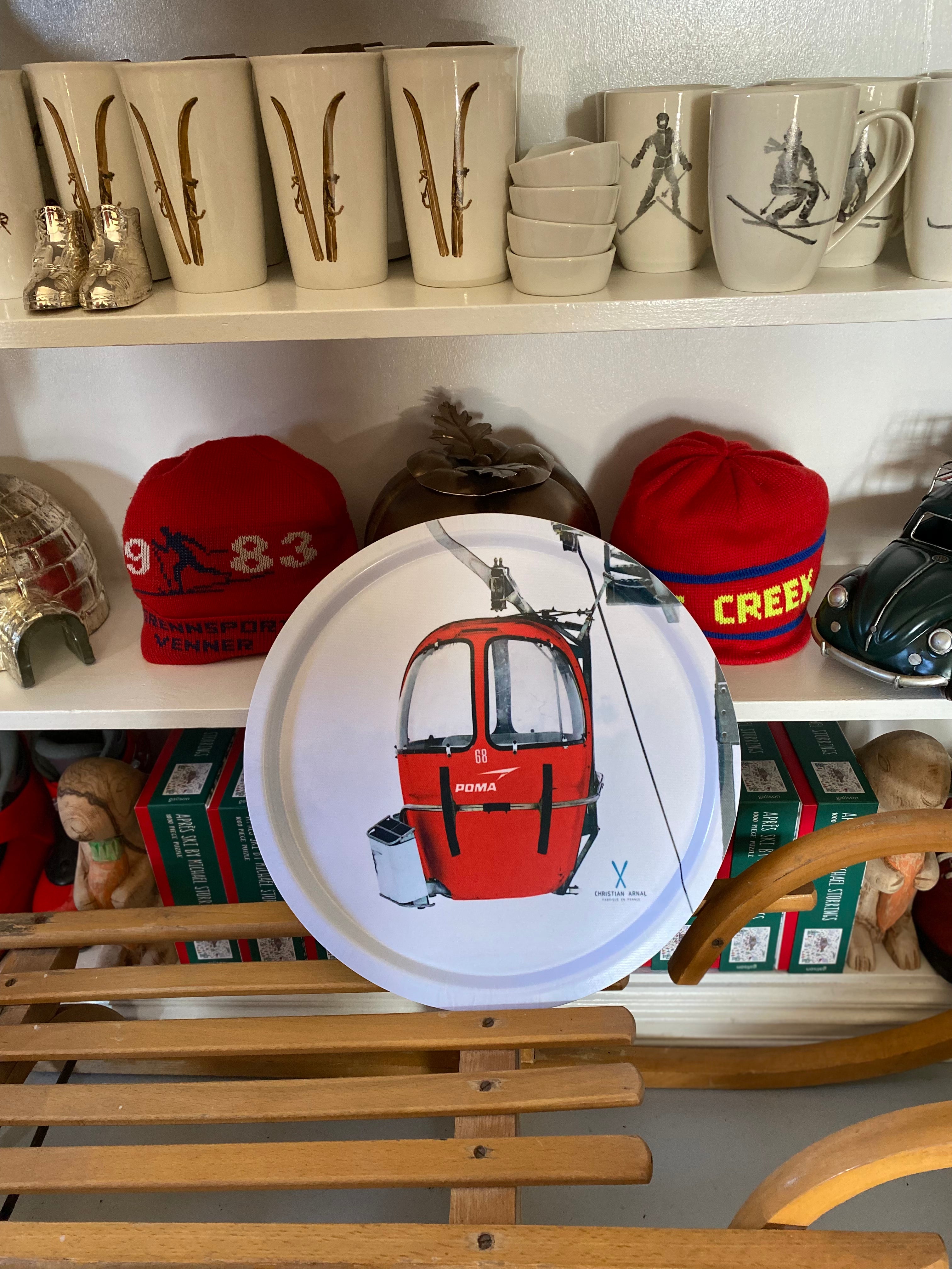 Photo of a Red Vintage Gondola printed onto a Round White Serving Tray, resting on a vintage wooden sled in front of a white bookshelf filled with snow related products