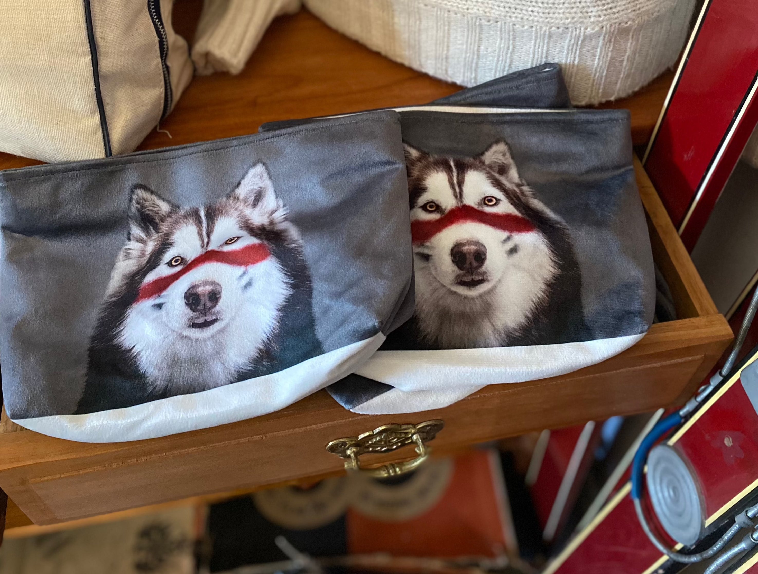 Pencil Case Makeup Bag sitting on a wooden table printed with a photo of a husky dog with a red stripe across its face on a grey background