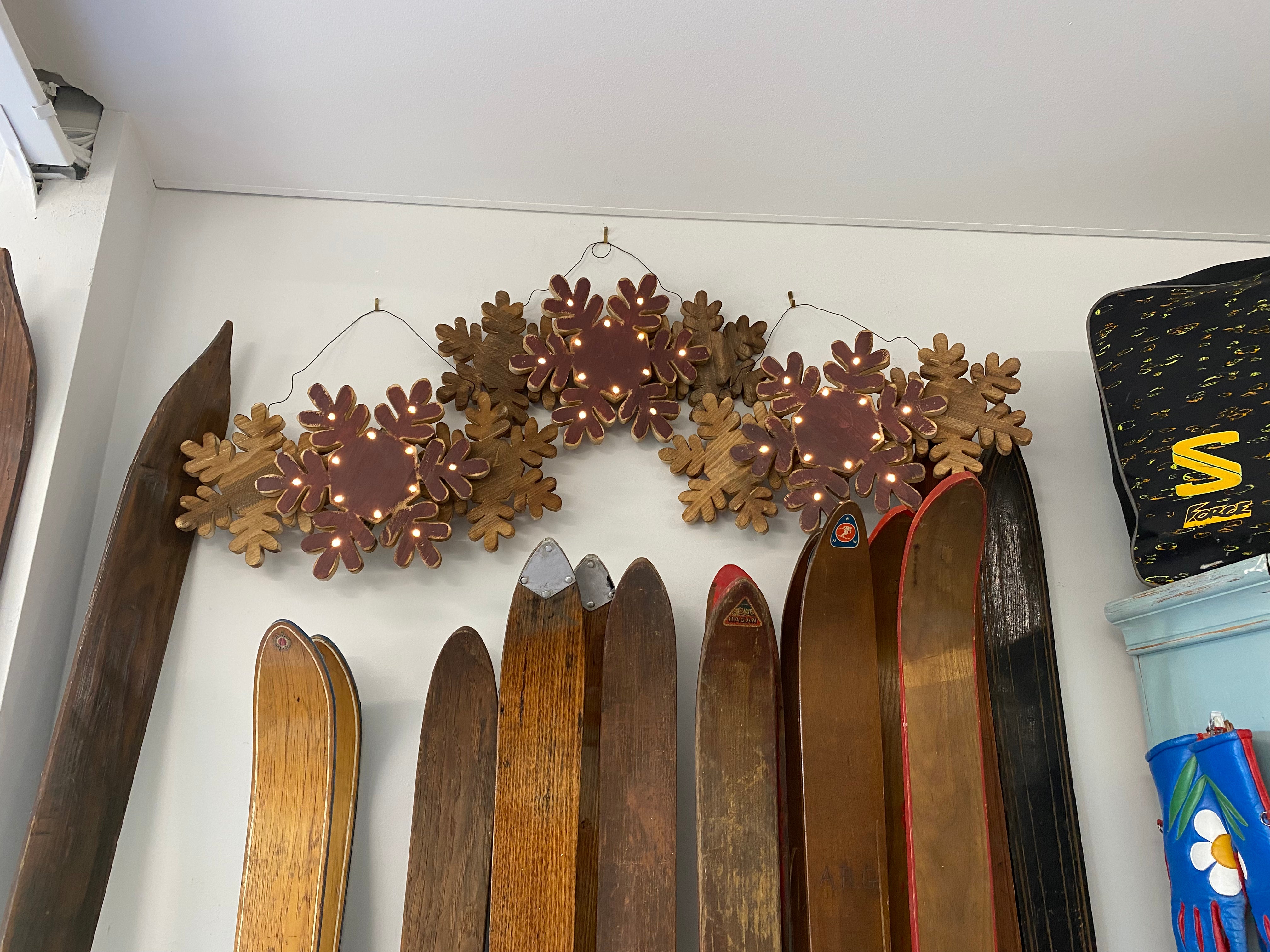 3 Wood snowflake wall decor with Led lights shown mid flash up on a white wall with 3 HAM Rabbit Prints & wooden skis underneath the snowflakes